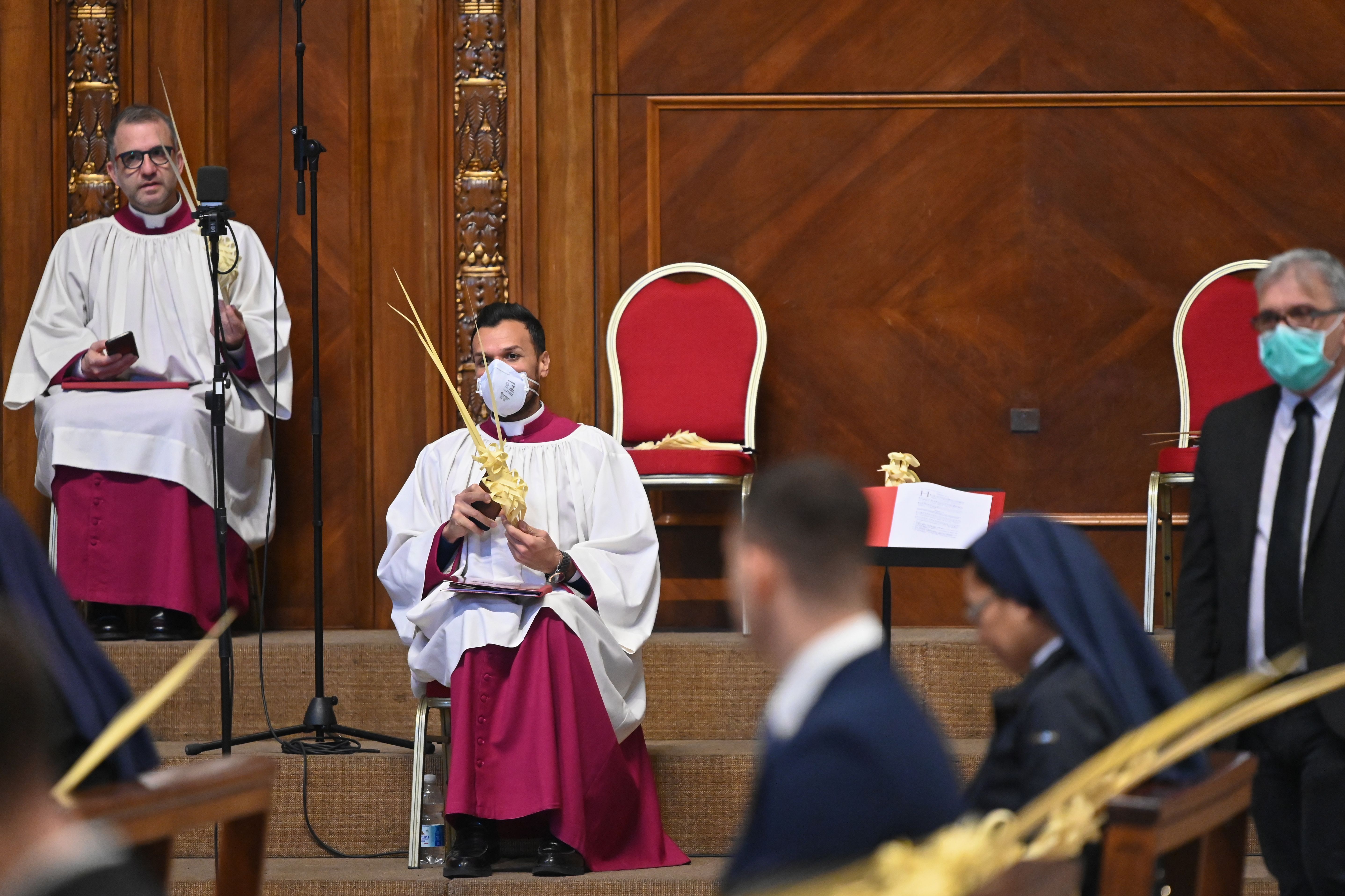 A prelate wearing a face mask holds a palm branch as attendees wait for the start of the Pope's Palm Sunday Mass behind closed doors in St. Peter's Basilica