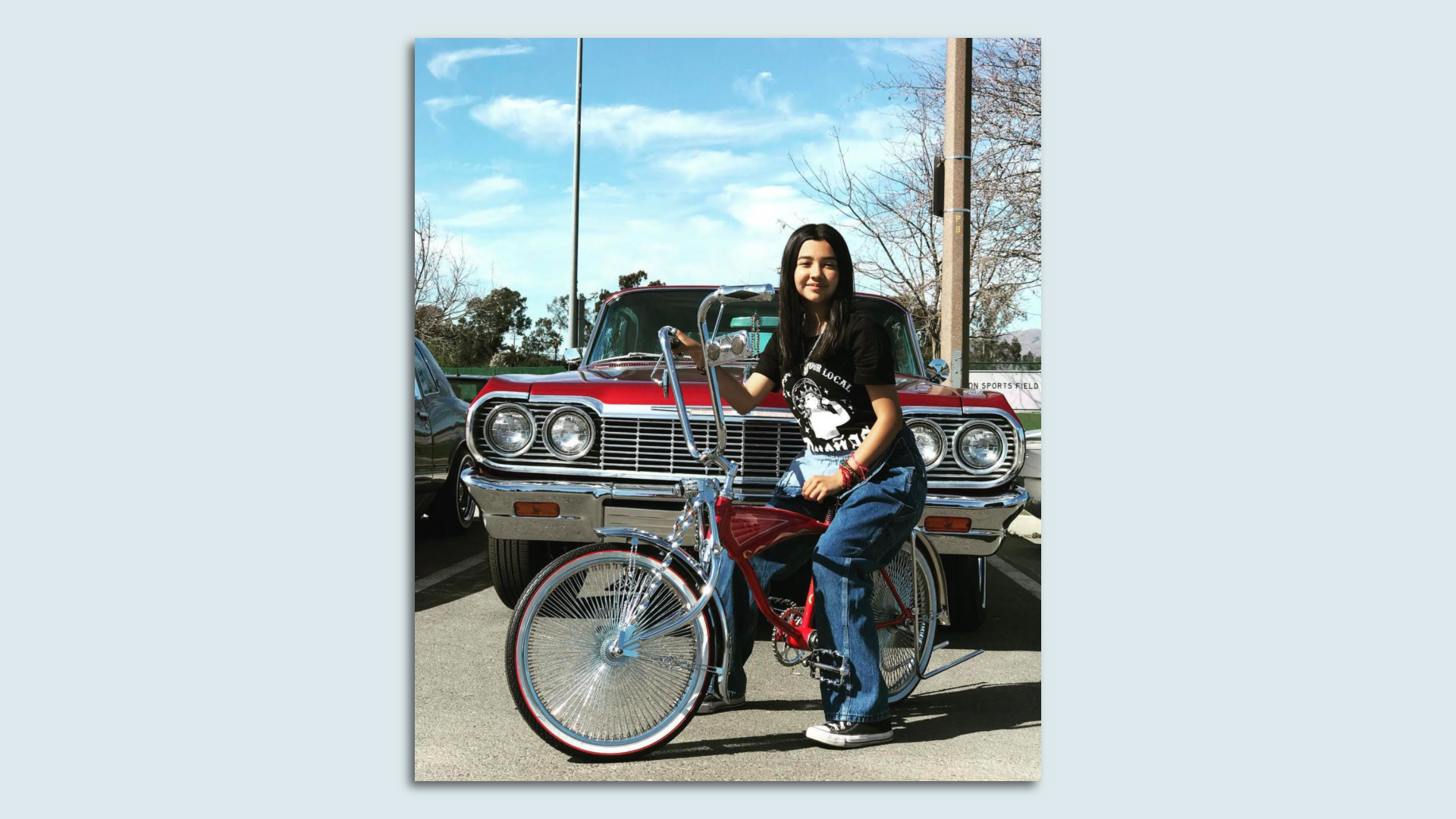 a young girl sits atop her custom lowrider bicycle which is shiny red with chrome details and long handlebars
