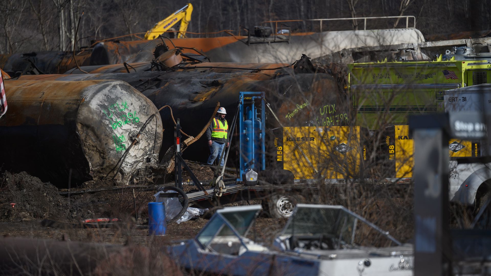 Photo of a derailed train car as a worker walks around the site