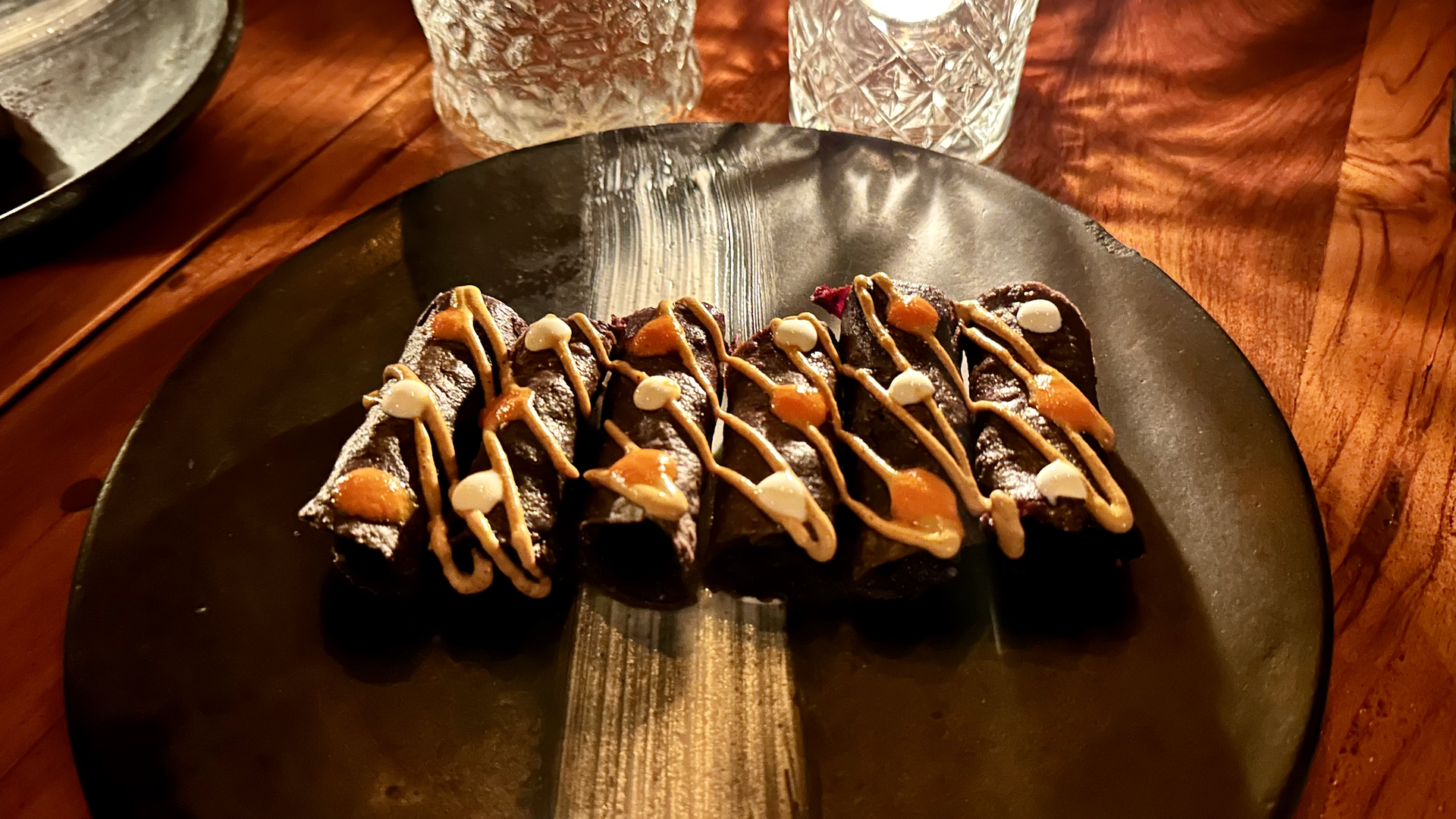 Six tacos with dark tortillas on a black plate