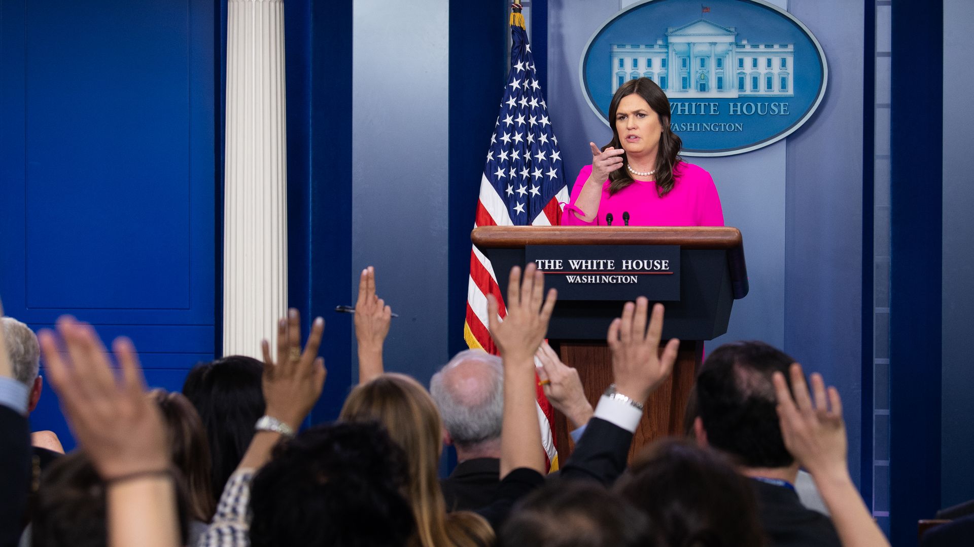 Sarah Sanders in a pink jacket a the White House briefing room stand