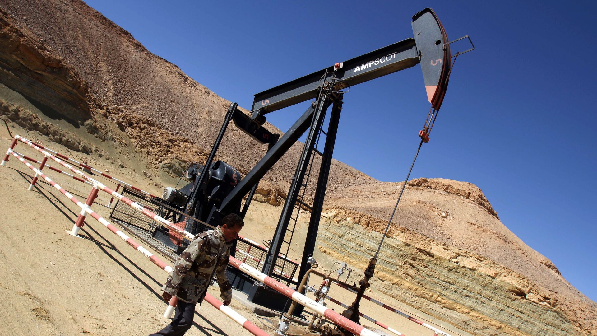 A Libyan security member walks by an oil drill.