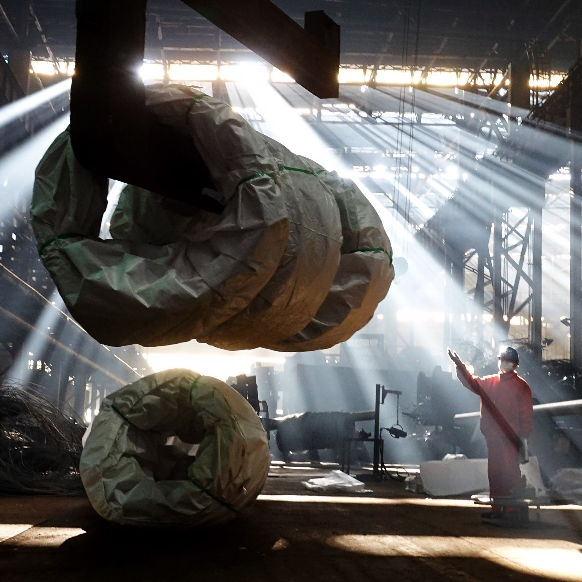worker on factory floor below suspended steel coil