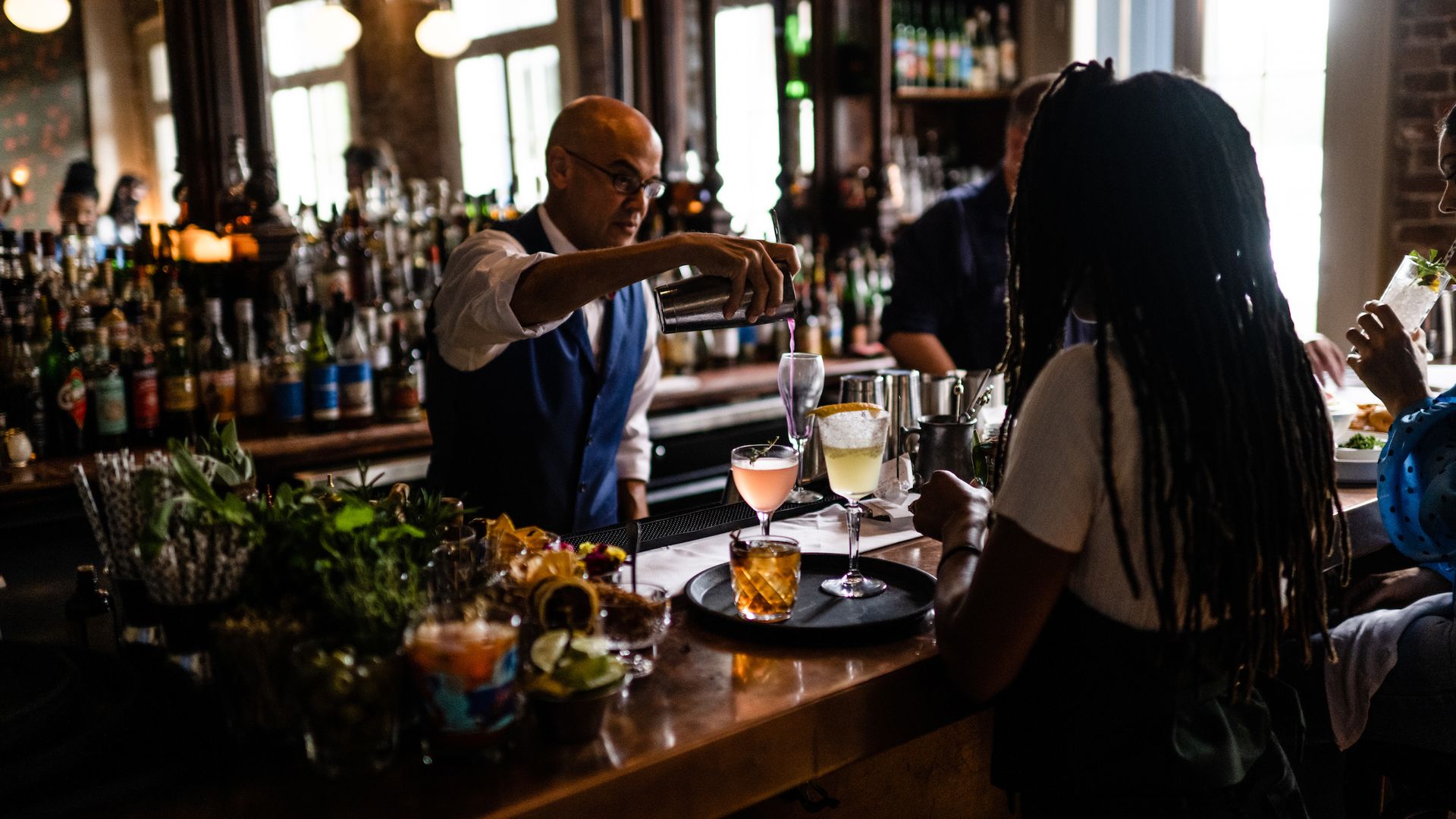 Photo shows Chris Hannah pouring a drink out of a shaker a customer seated at the bar of Jewel of the South. 