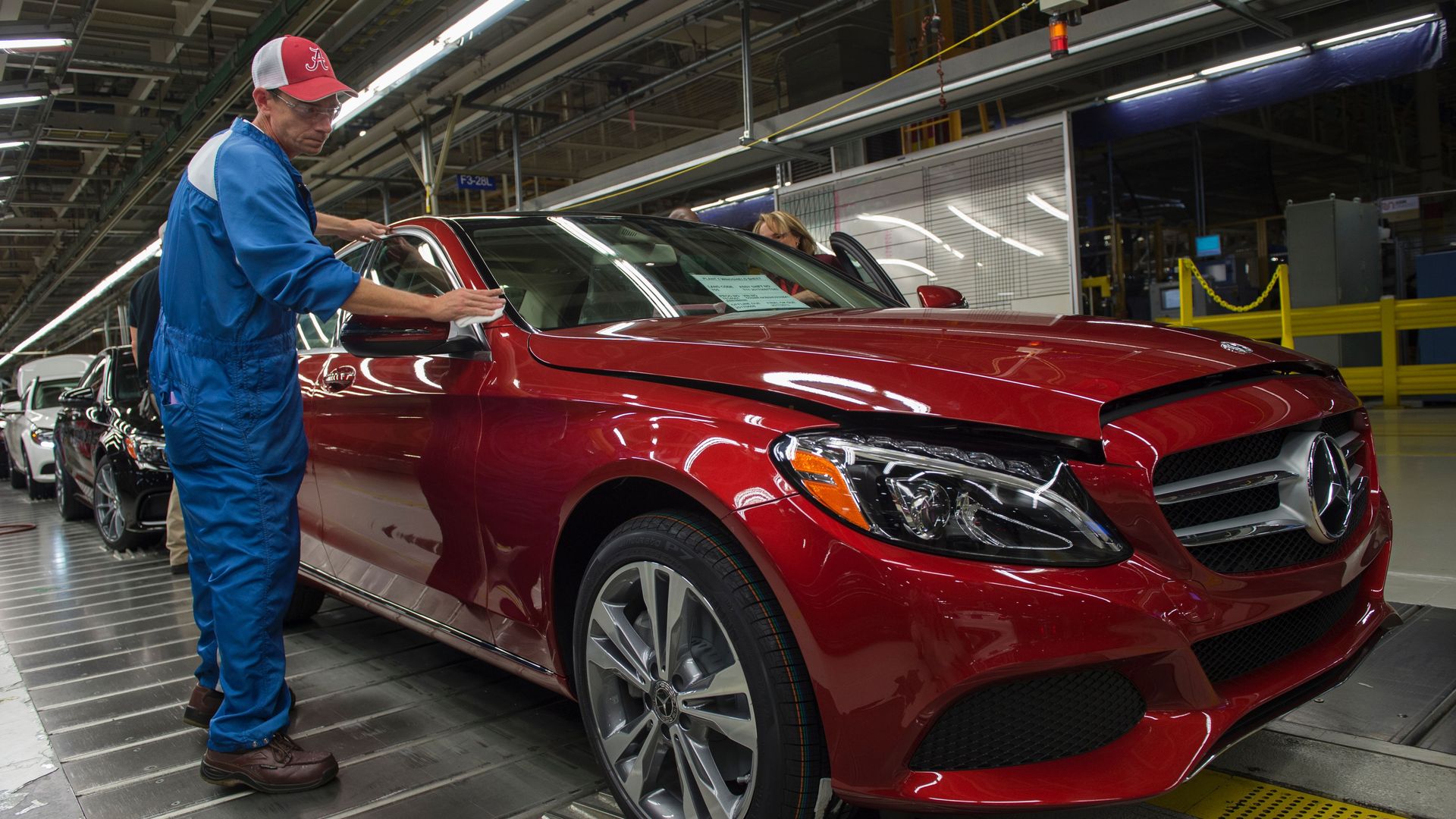A factory worker shines a red car on an assembly line