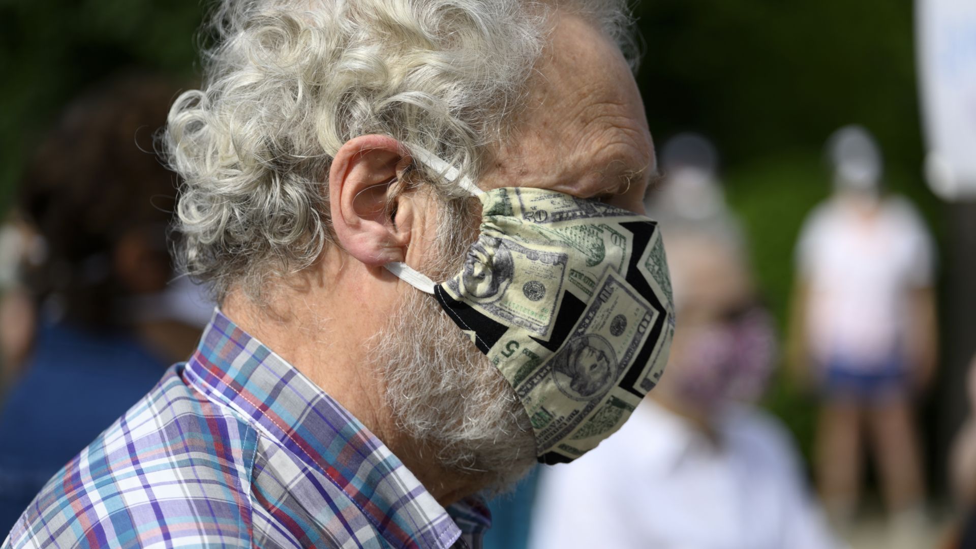 A person wearing a face mask with a U.S. currency print.