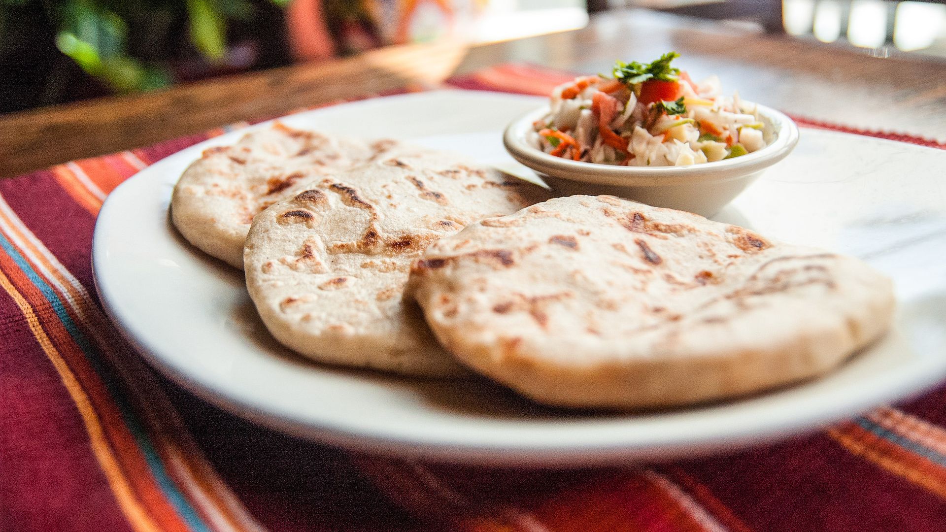 Three pupusas on a white plate with cortido slaw on a table at El Tamarindo