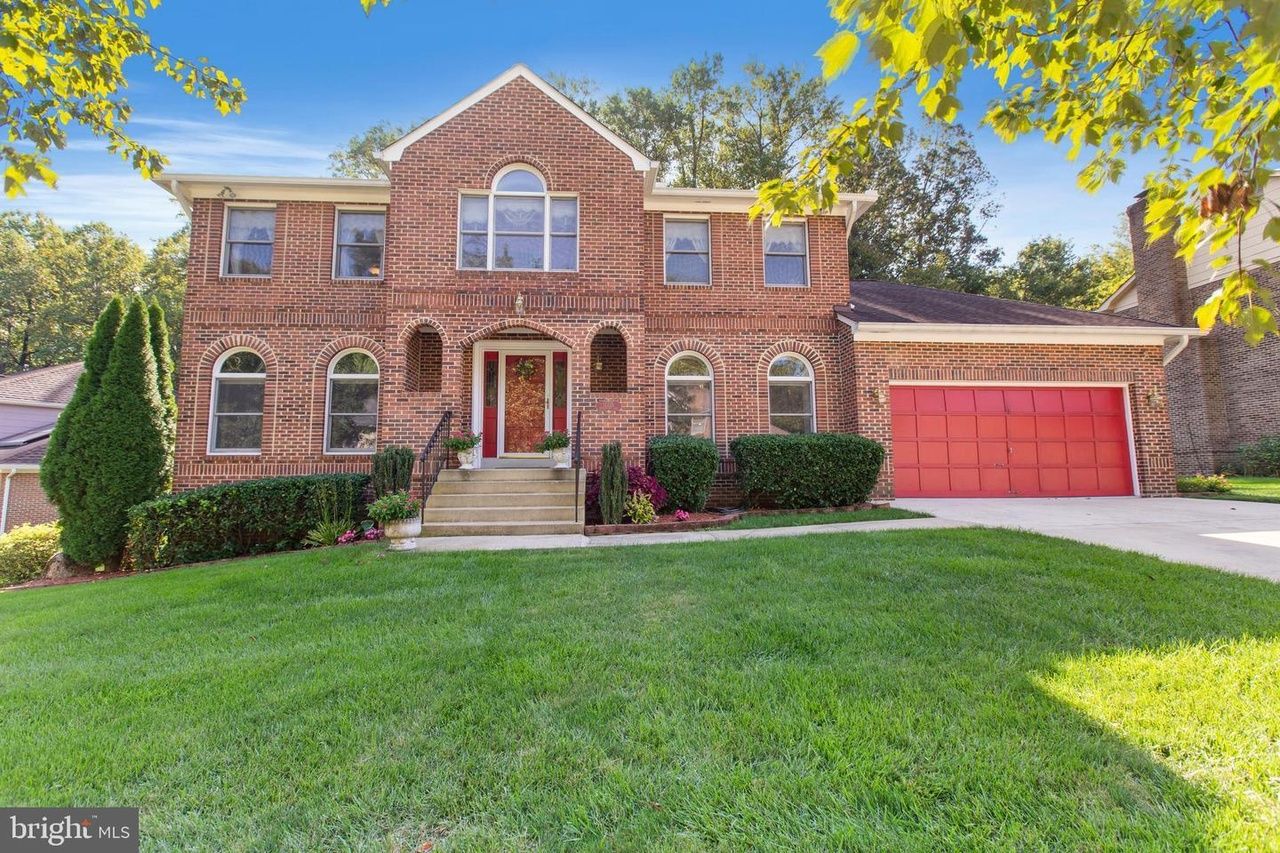 An all brick colonial home with a bright green yard and red garage door.