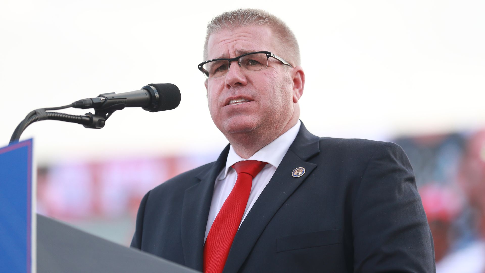 Photo of a man behind a microphone talking to a crowd. 