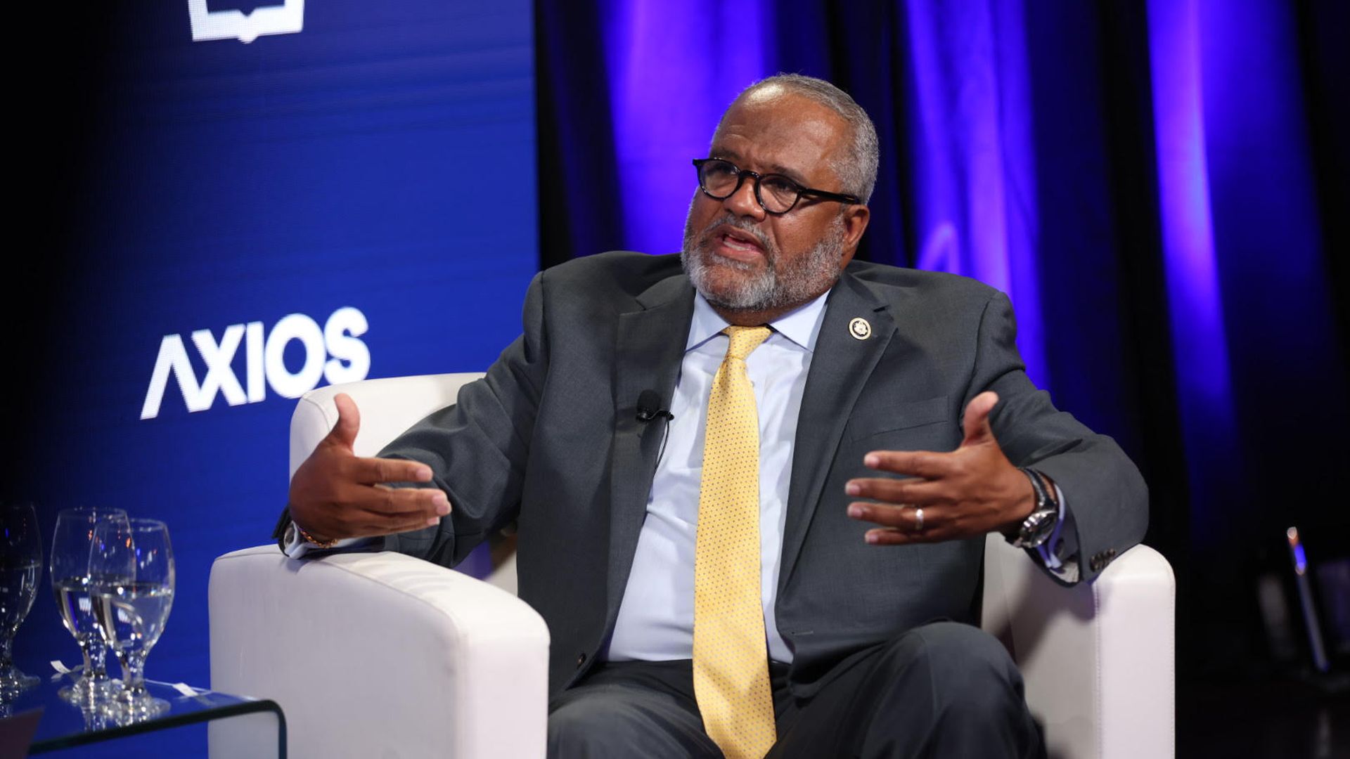 Rep. Troy Carter speaks while sitting in a white chair in front of a blue backdrop with white Axios logos.