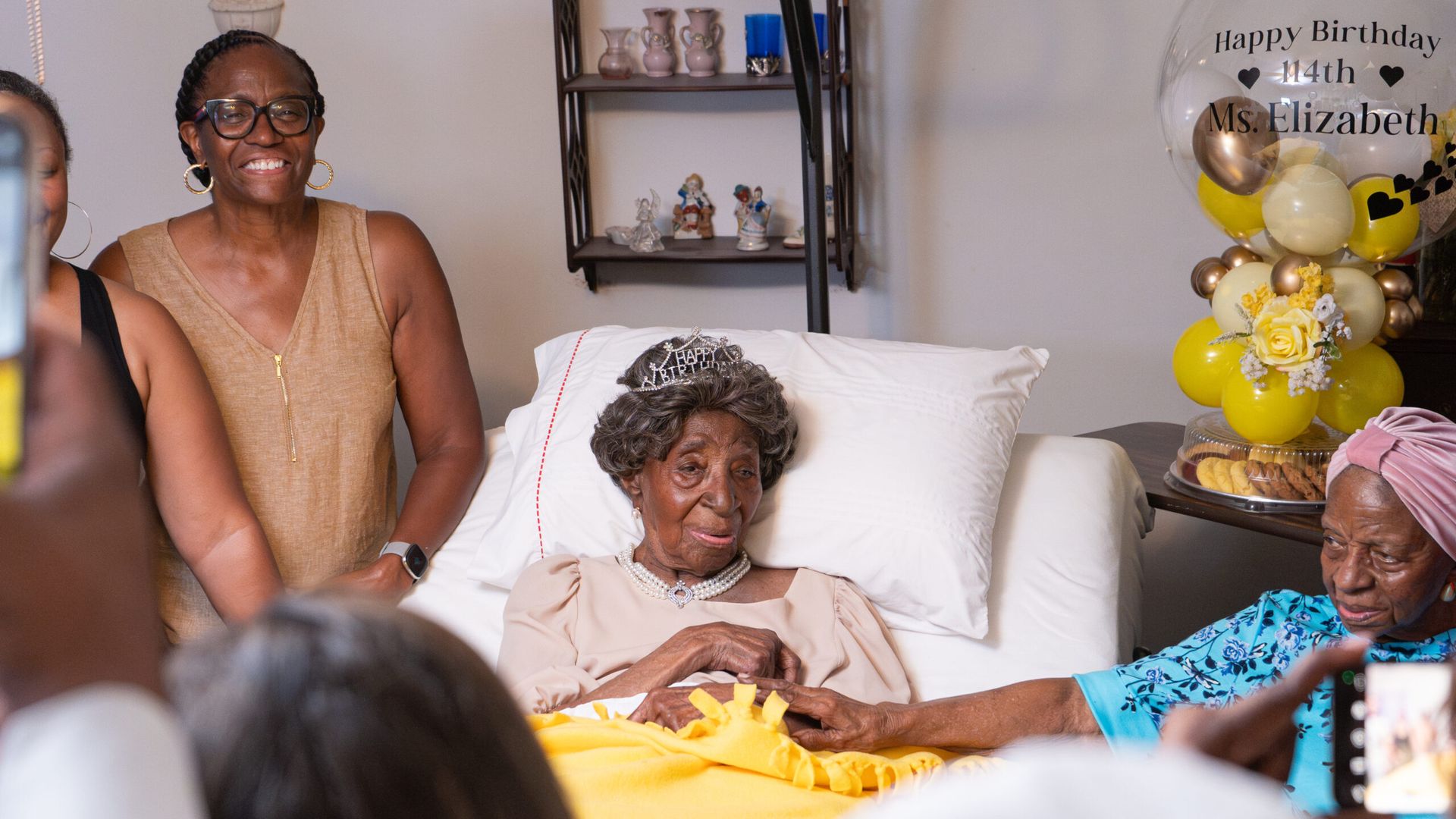Elizabeth Francis, 114, is surrounded by family while laying in bed wearing a tiara that says "Happy Birthday"