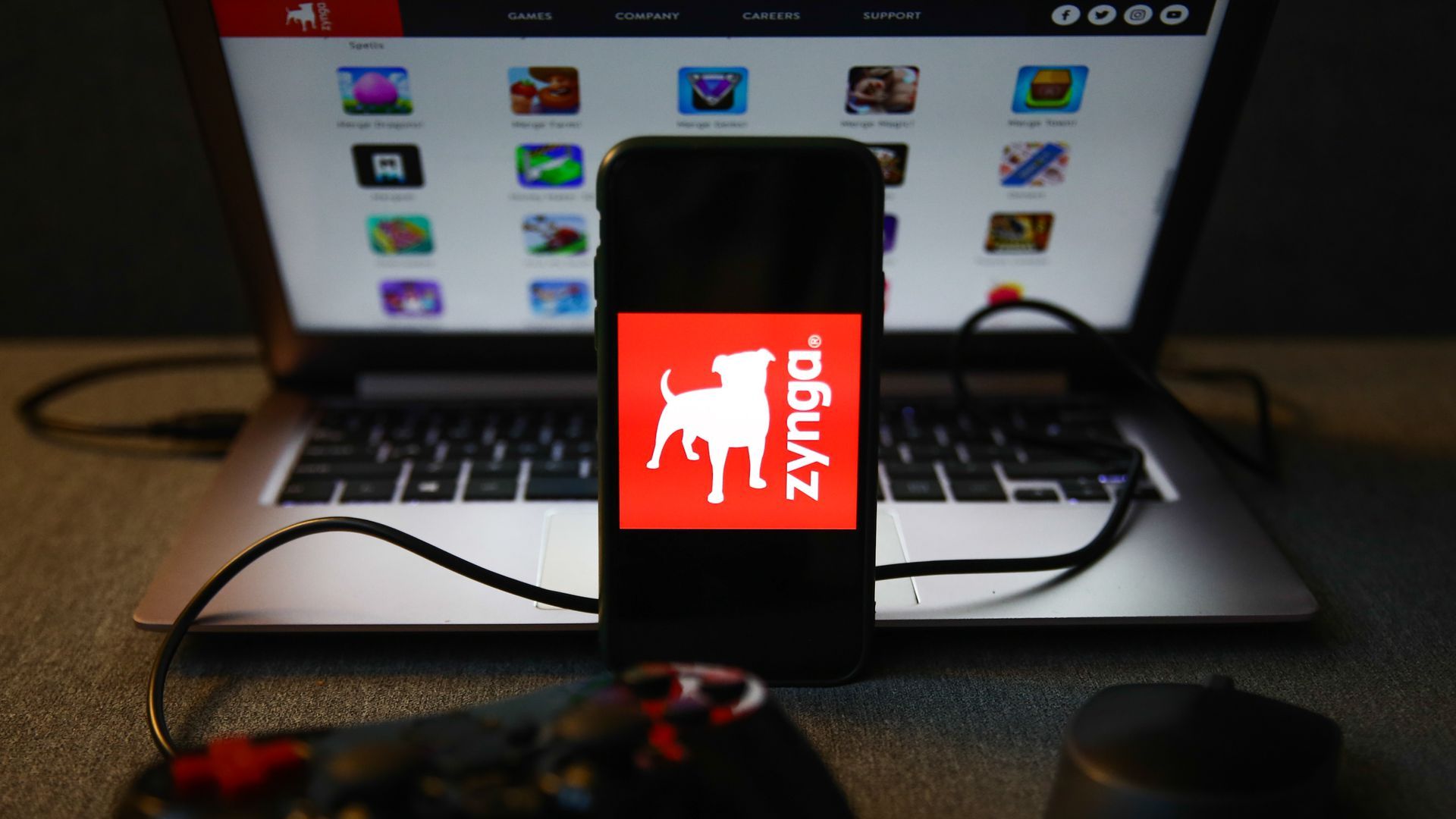 A photo Illustration of the Zynga logo on a smartphone in front of a Mac with the Zynga website