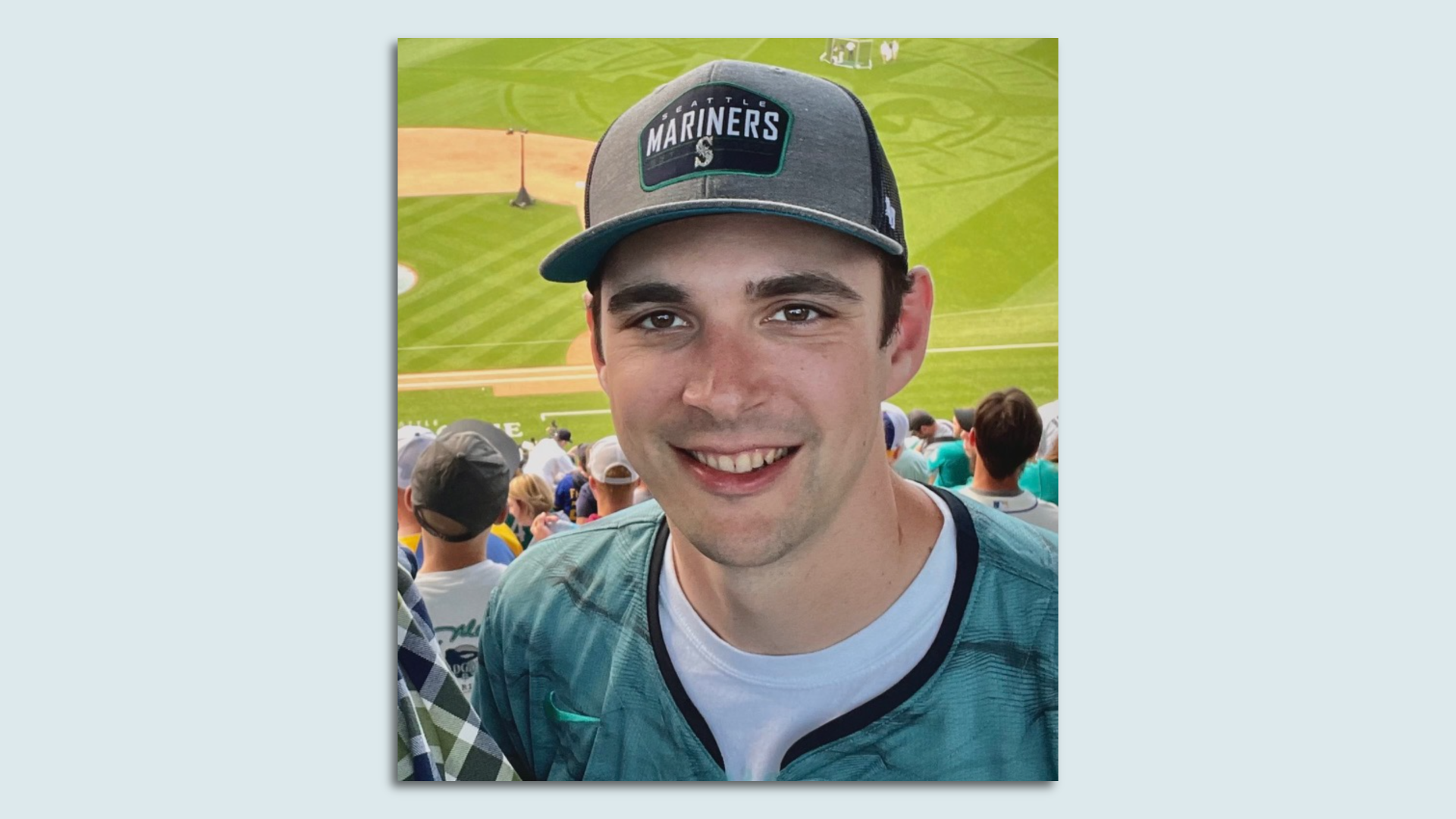 A young man in a Mariners hat in front of a baseball game. 