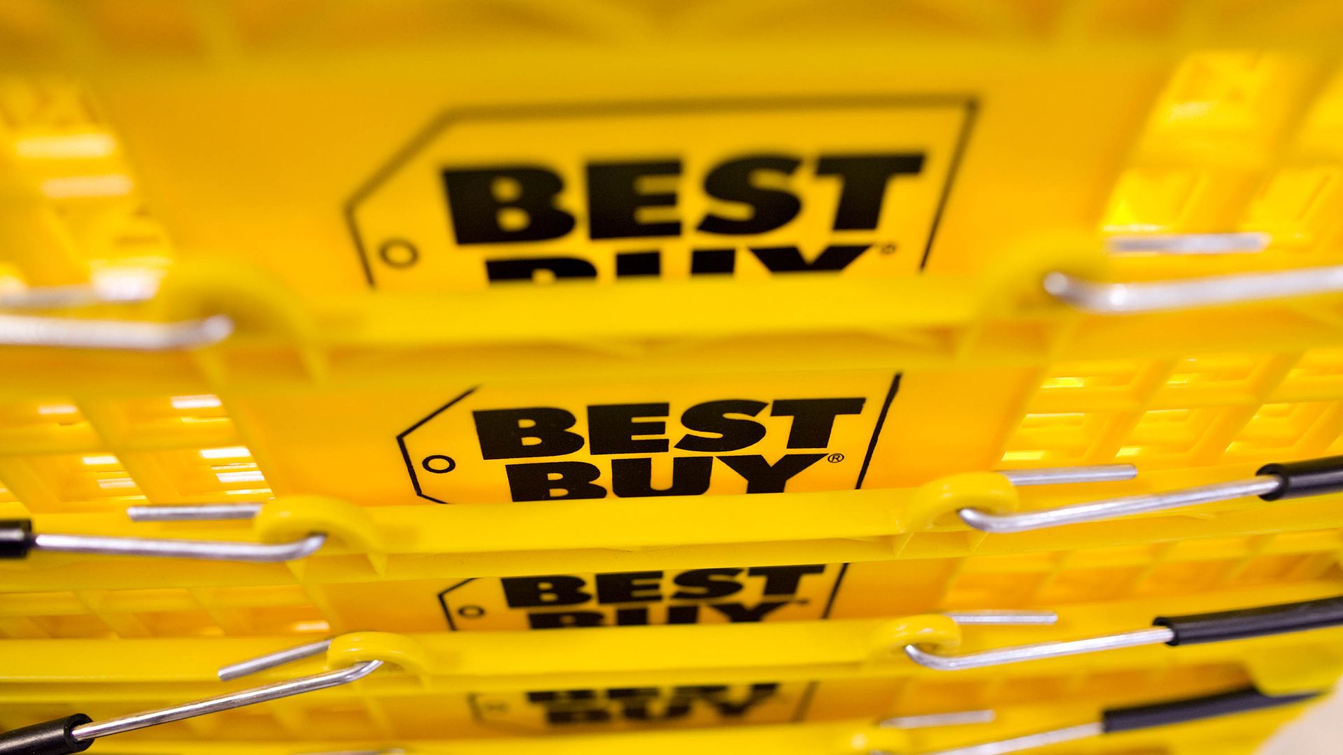 Close-up of stacked yellow Best Buy shopping baskets with black handles and the Best Buy logo prominently displayed on each basket.
