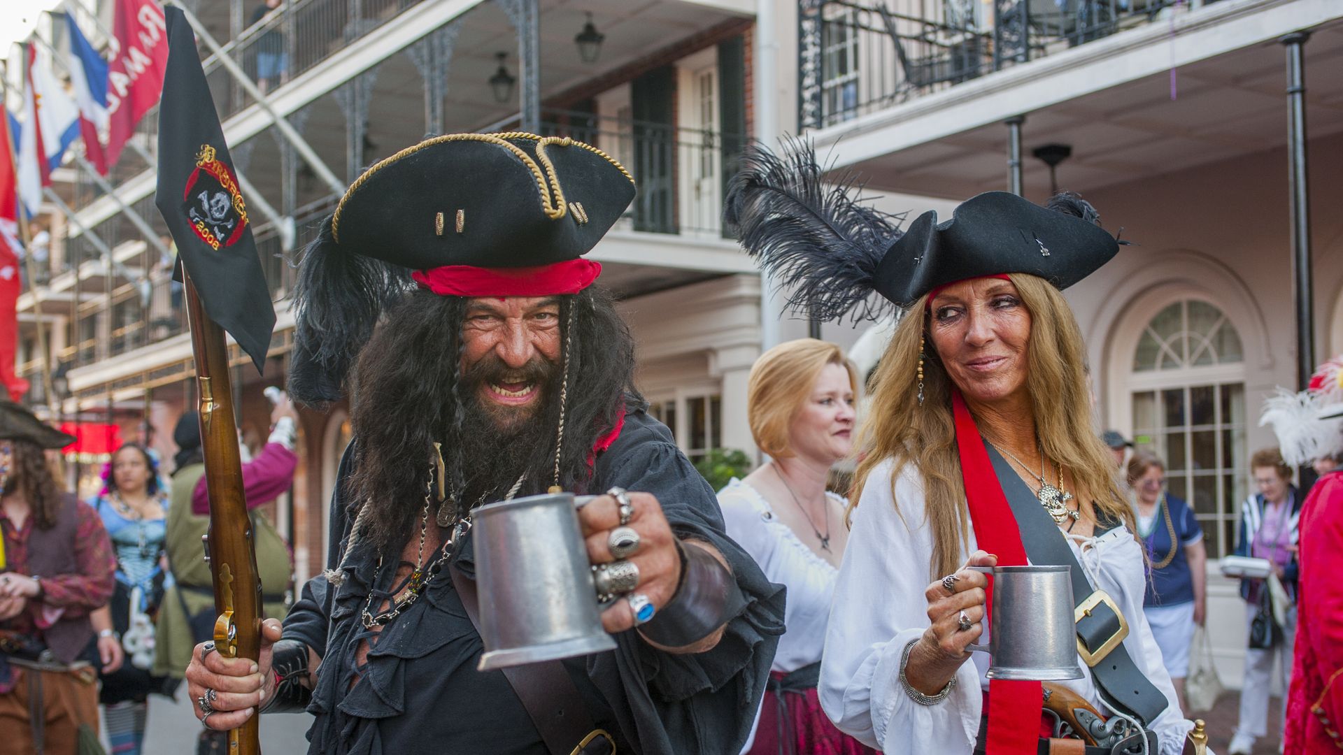 A man dressed like a pirate gestures to the camera with a metal mug while marching in the French Quarter.