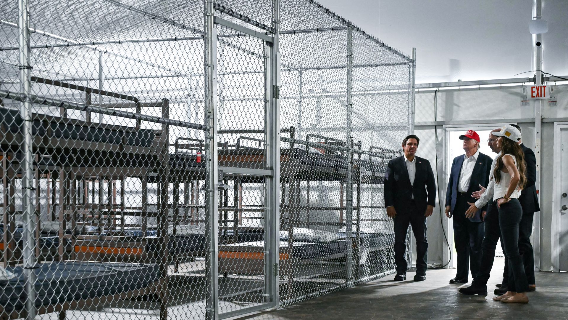 Officials standing in front of a large cage with beds inside. 