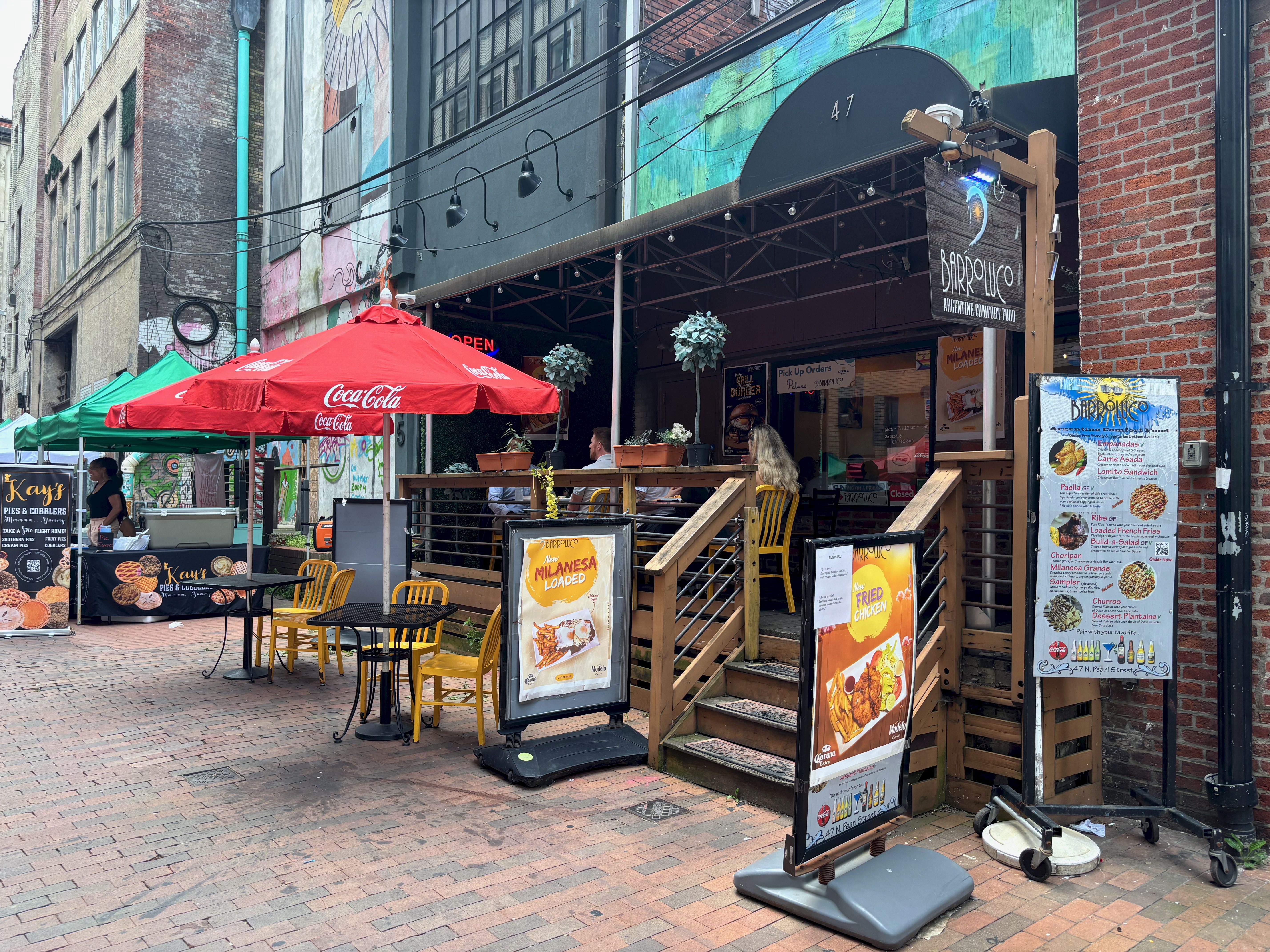 The exterior of the restaurant, with a patio and two chairs with umbrellas and steps leading inside.
