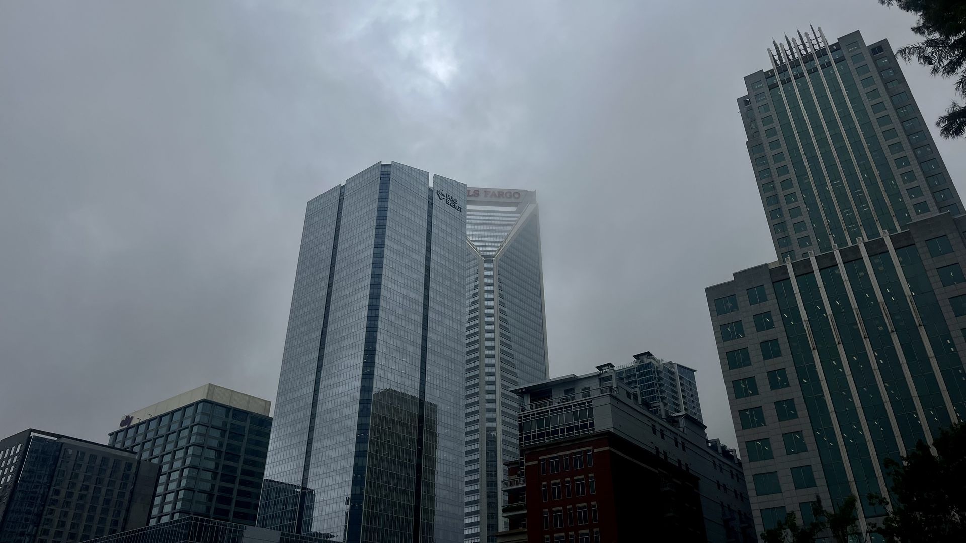 Overcast sky above a cityscape with tall glass and concrete office buildings, including one with the Wells Fargo logo partially obscured by clouds.