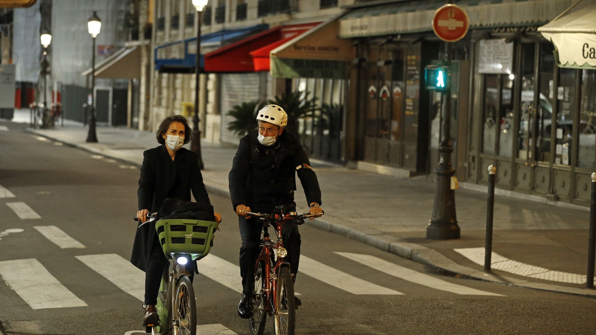 A couple wearing protective face masks ride their bicycle in a deserted street before the 9pm city-wide night time curfew during the coronavirus