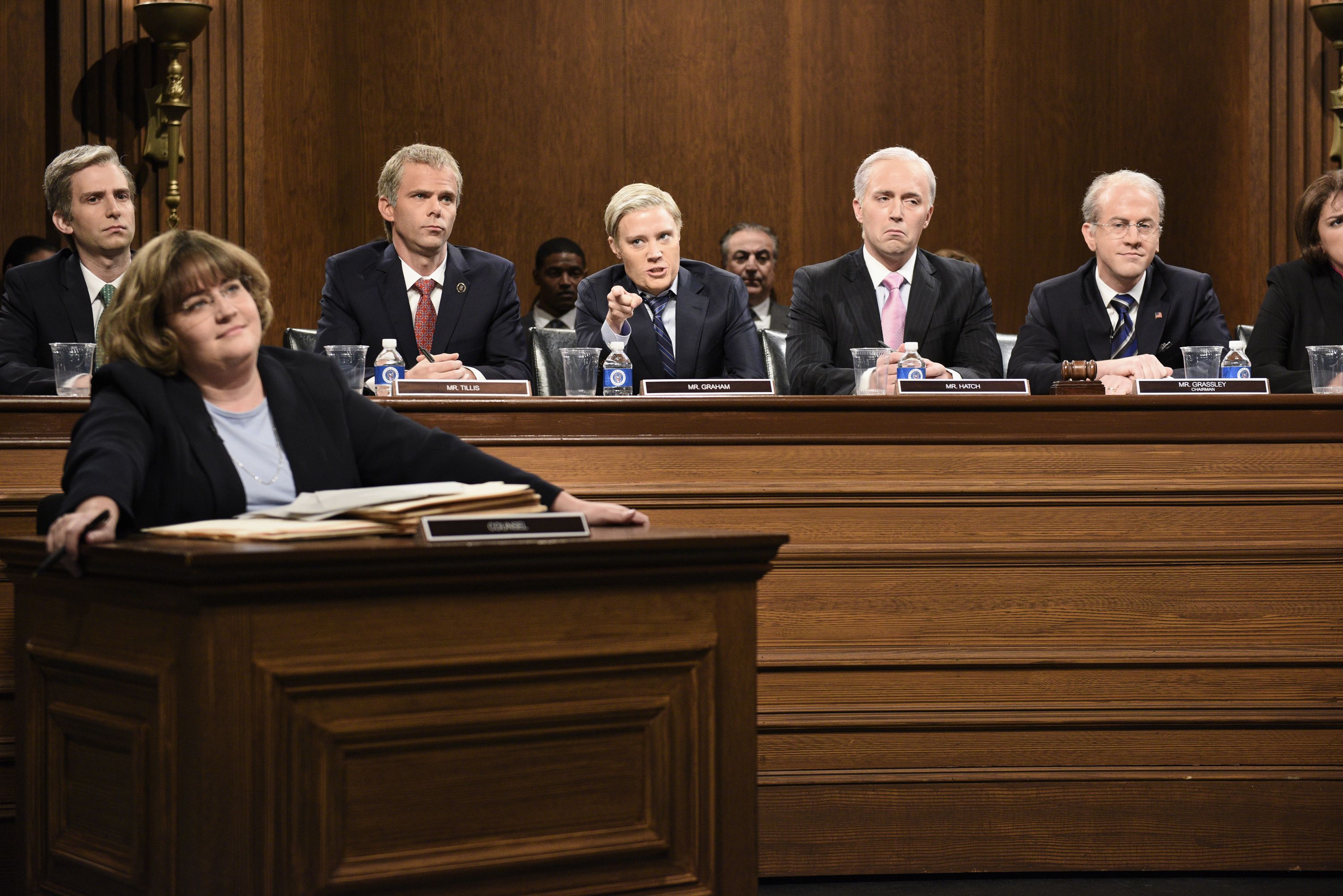 A woman sitting at a desk in front of a row of men. 
