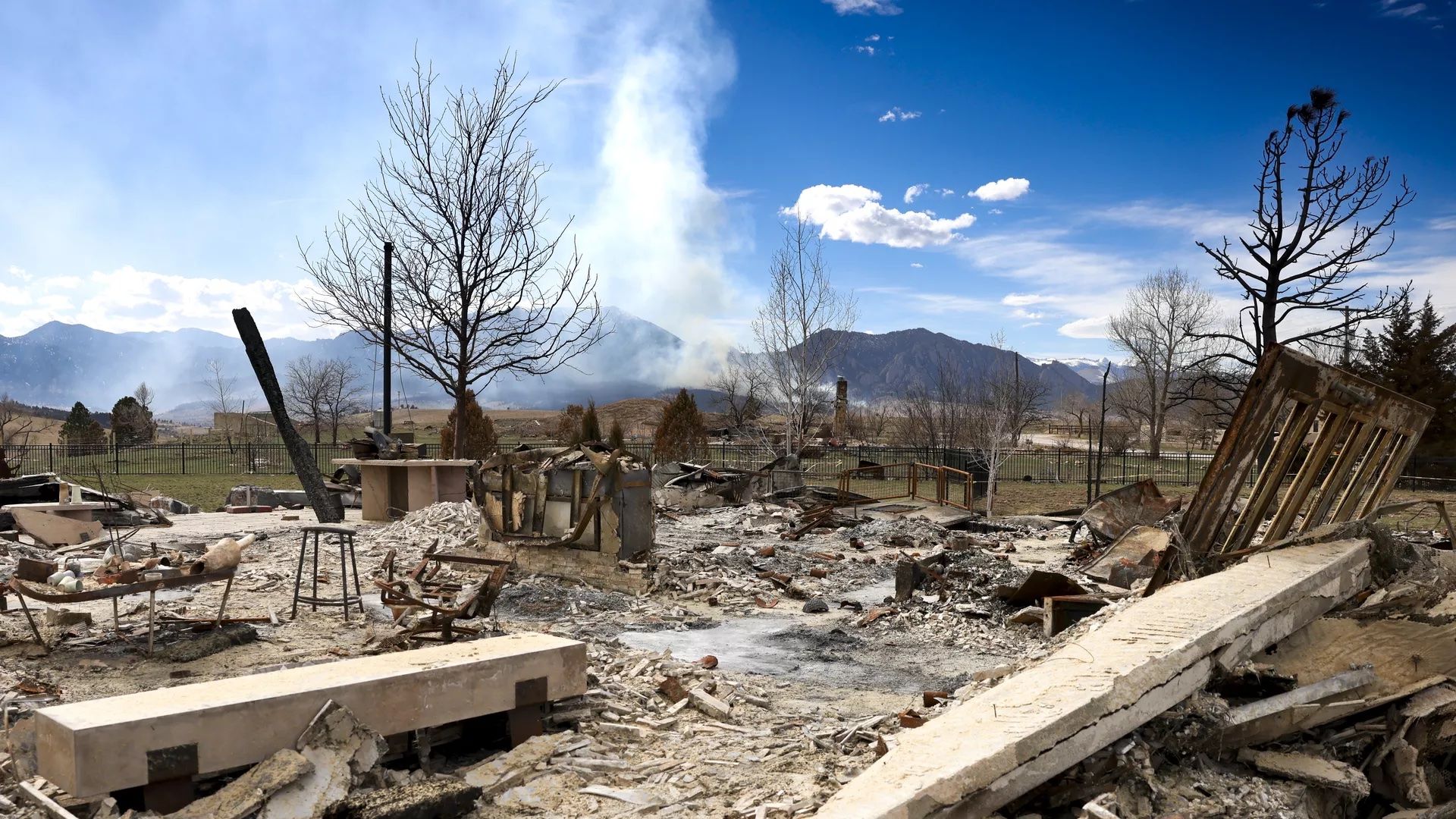 A home destroyed in the Marshall Fire sits in ruins as a new wildfire burns in the distance.