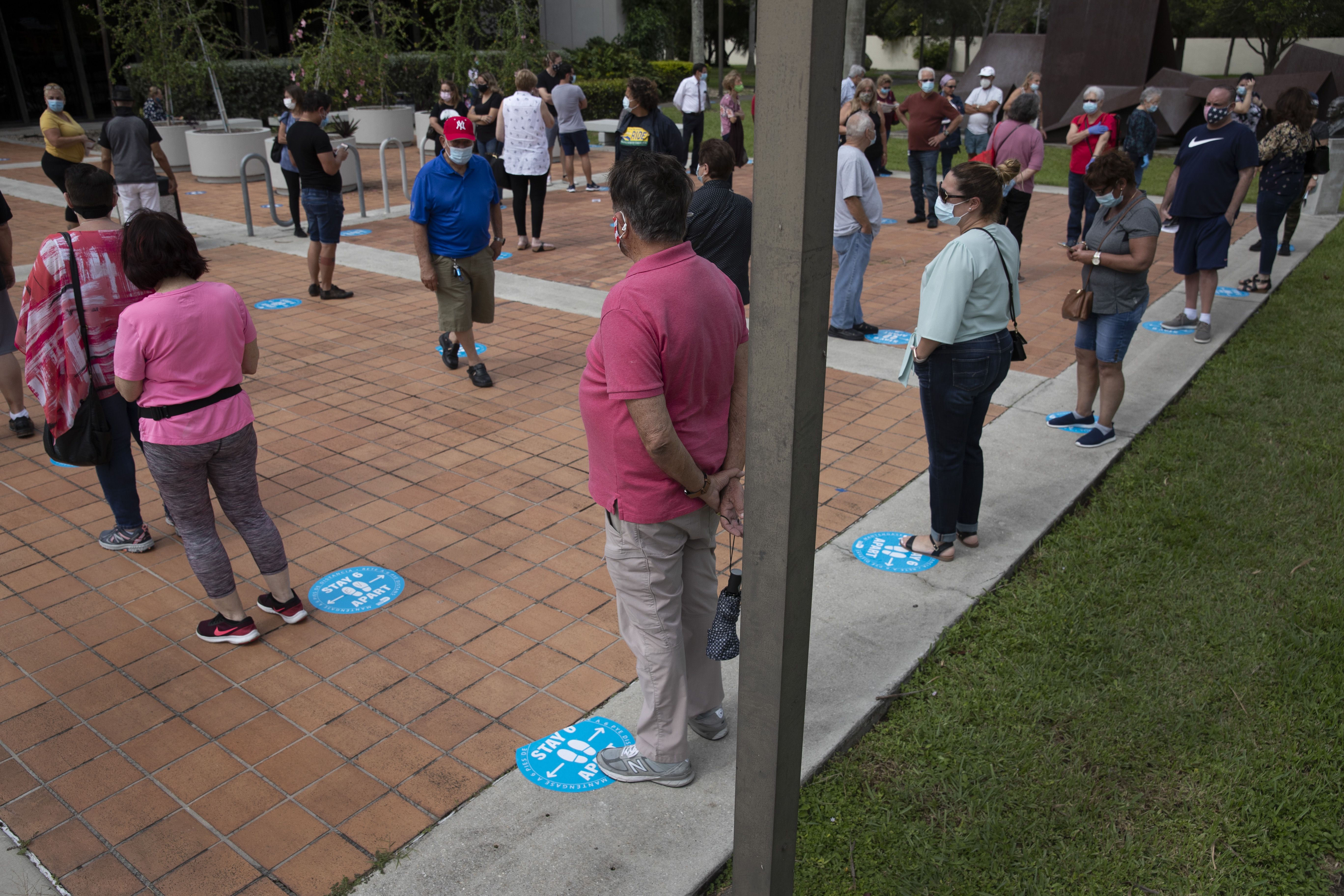 People stand on blue dots while socially distanced from each other outside 