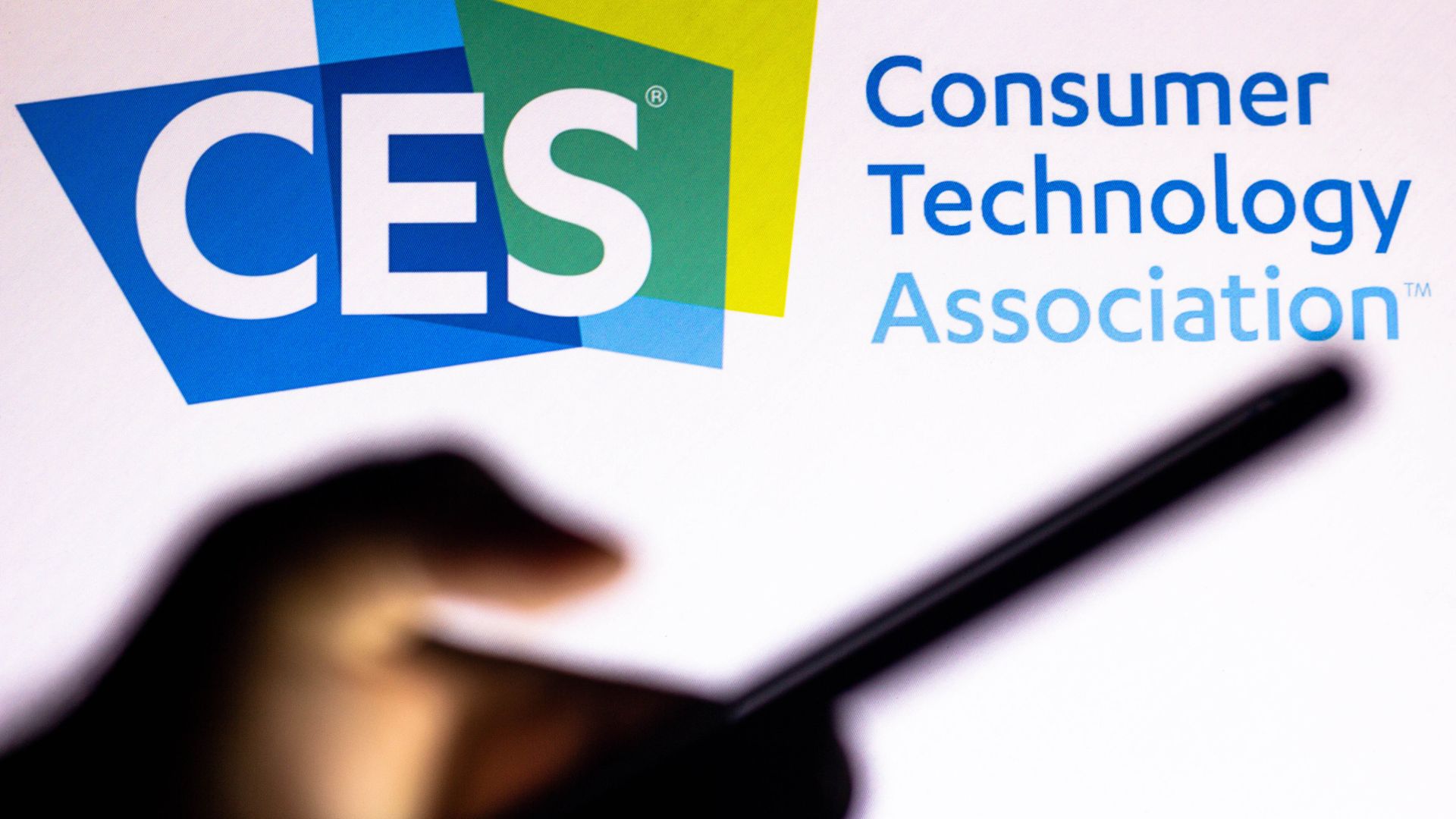 The shadow of a hand and smartphone are seen in front of the CES logo