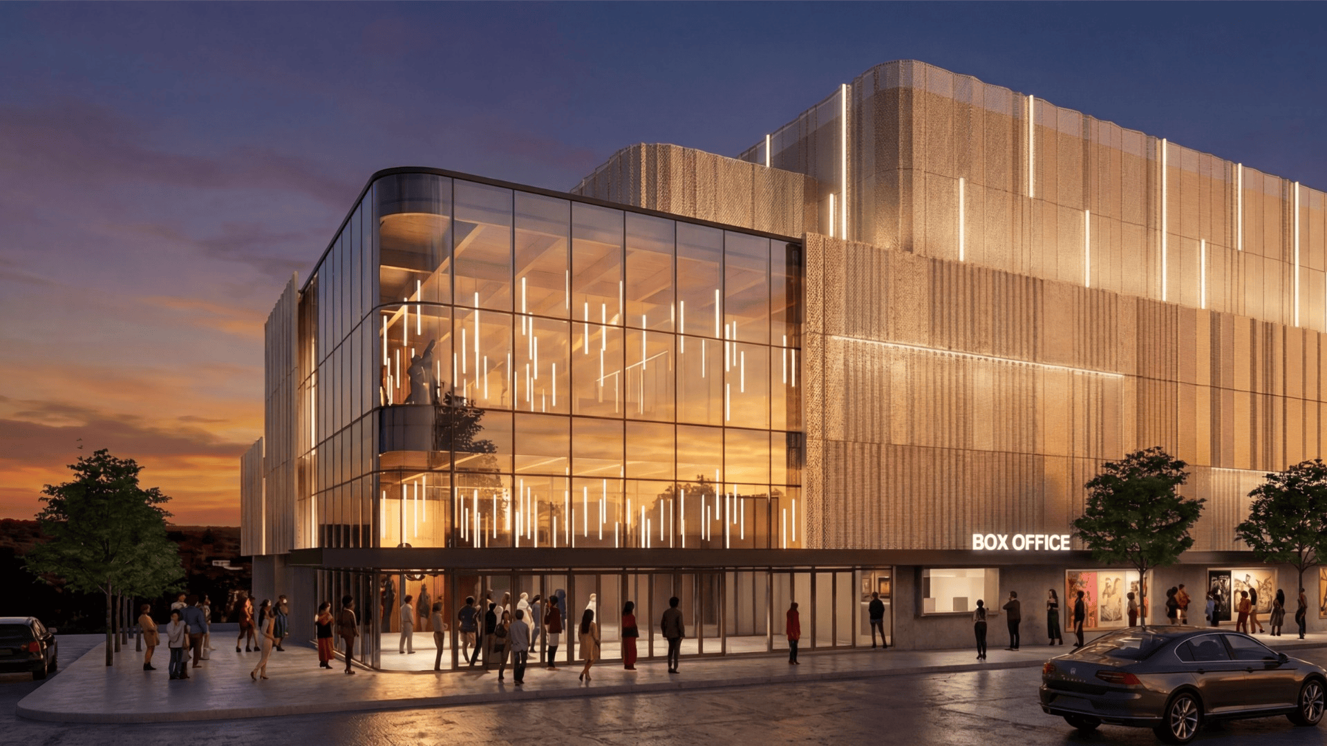 Modern glass-fronted theater at sunset with warm interior lights and vertical light strips on a textured facade. People stand outside the BOX OFFICE as a car drives by.