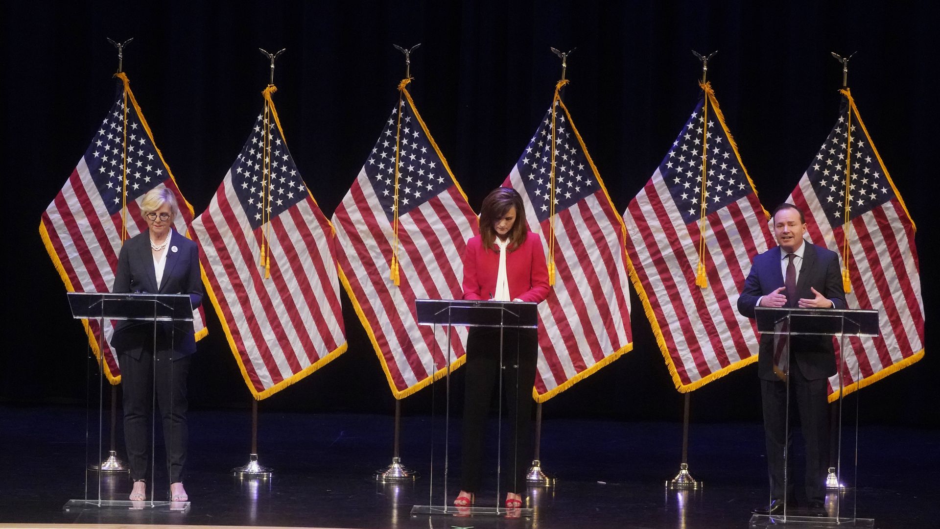 Three U.S. Senate candidates behind podiums and American flags.