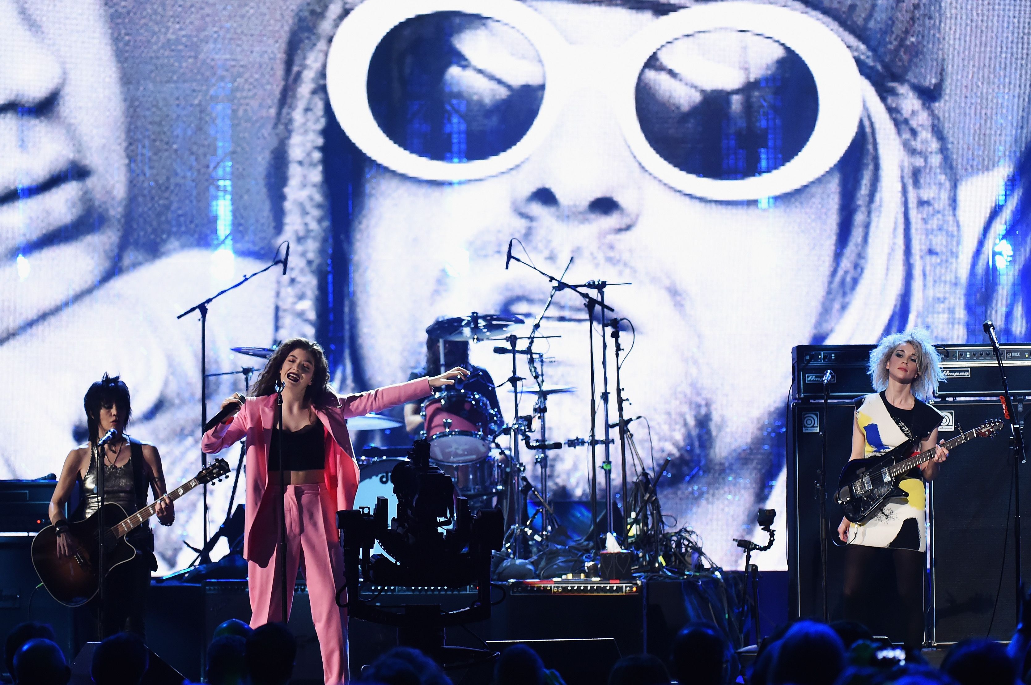 Joan Jett, Lorde and St. Vincent perform on stage with members of Nirvana as a photo of the legendary 1990s band is shown on a big screen behind them. 