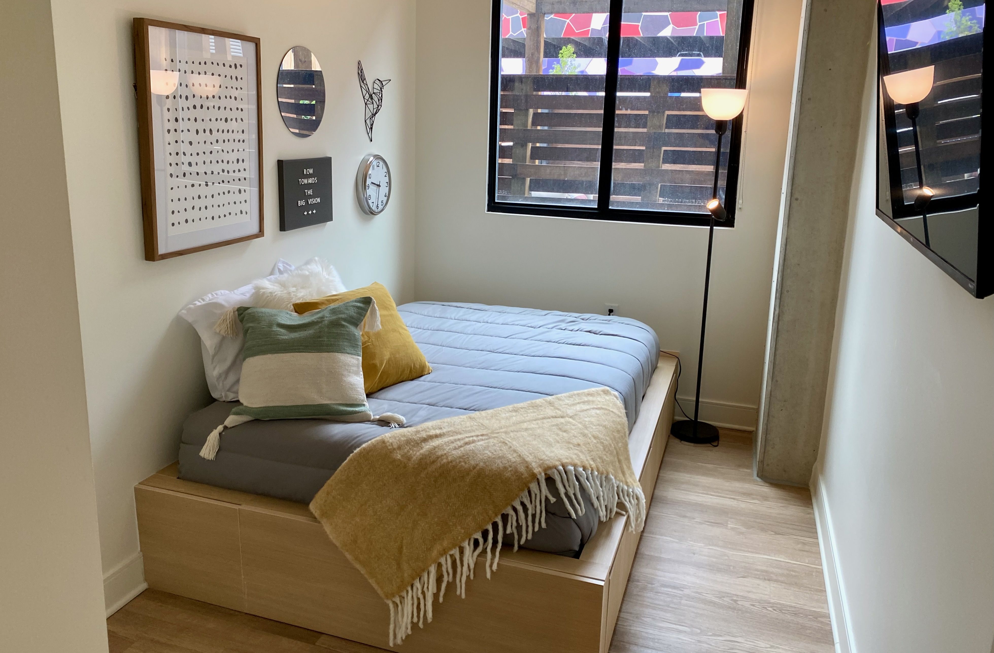 A bedroom with a full-sized bed, tall lamp, mounted TV and window
