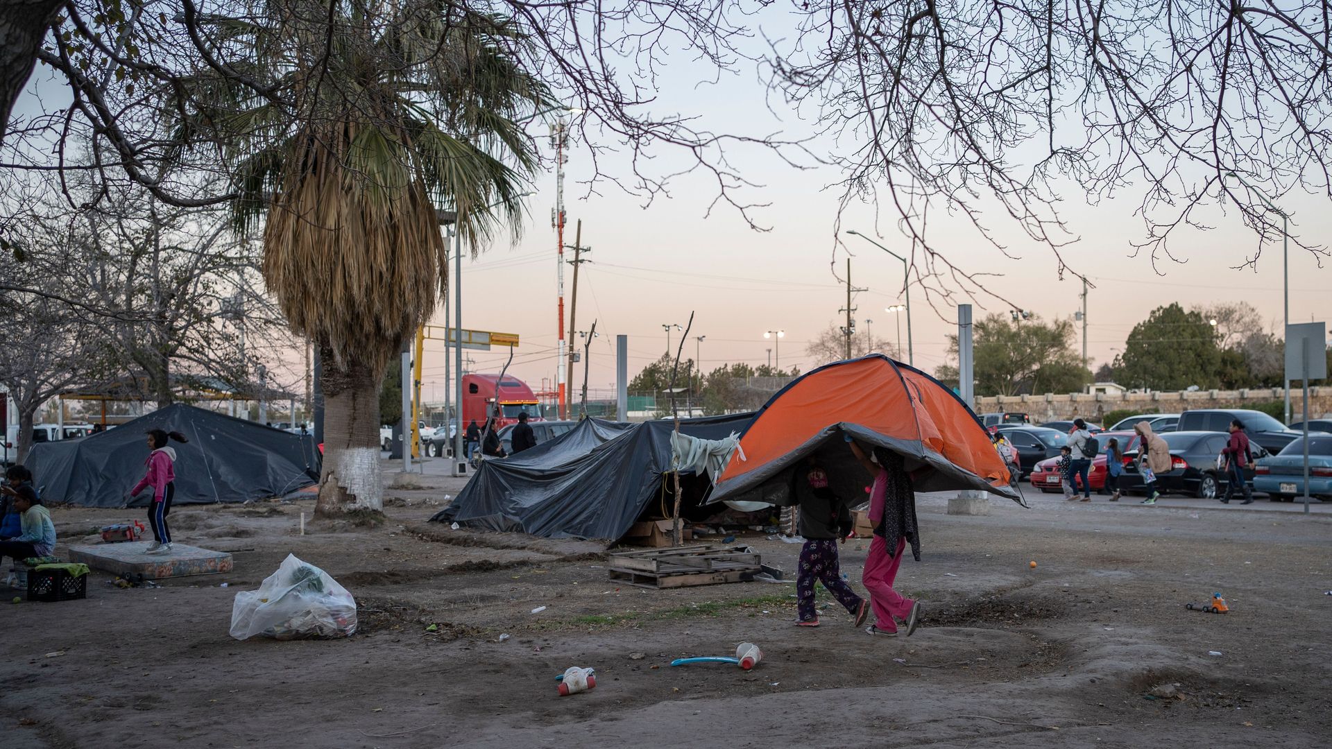 Girls carry a tent to across the campsite of asylum seekers