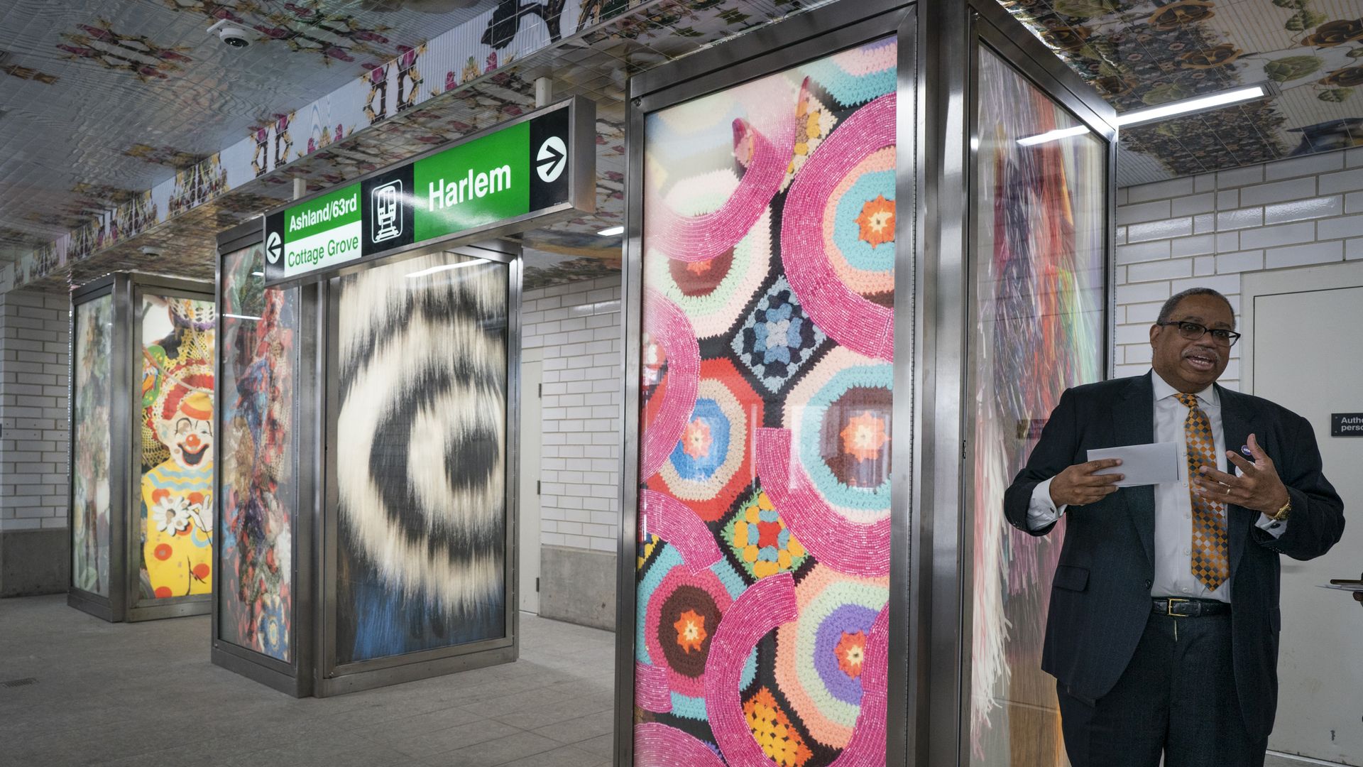 Multi-colored panels in a train station with a man in a suit to the right.