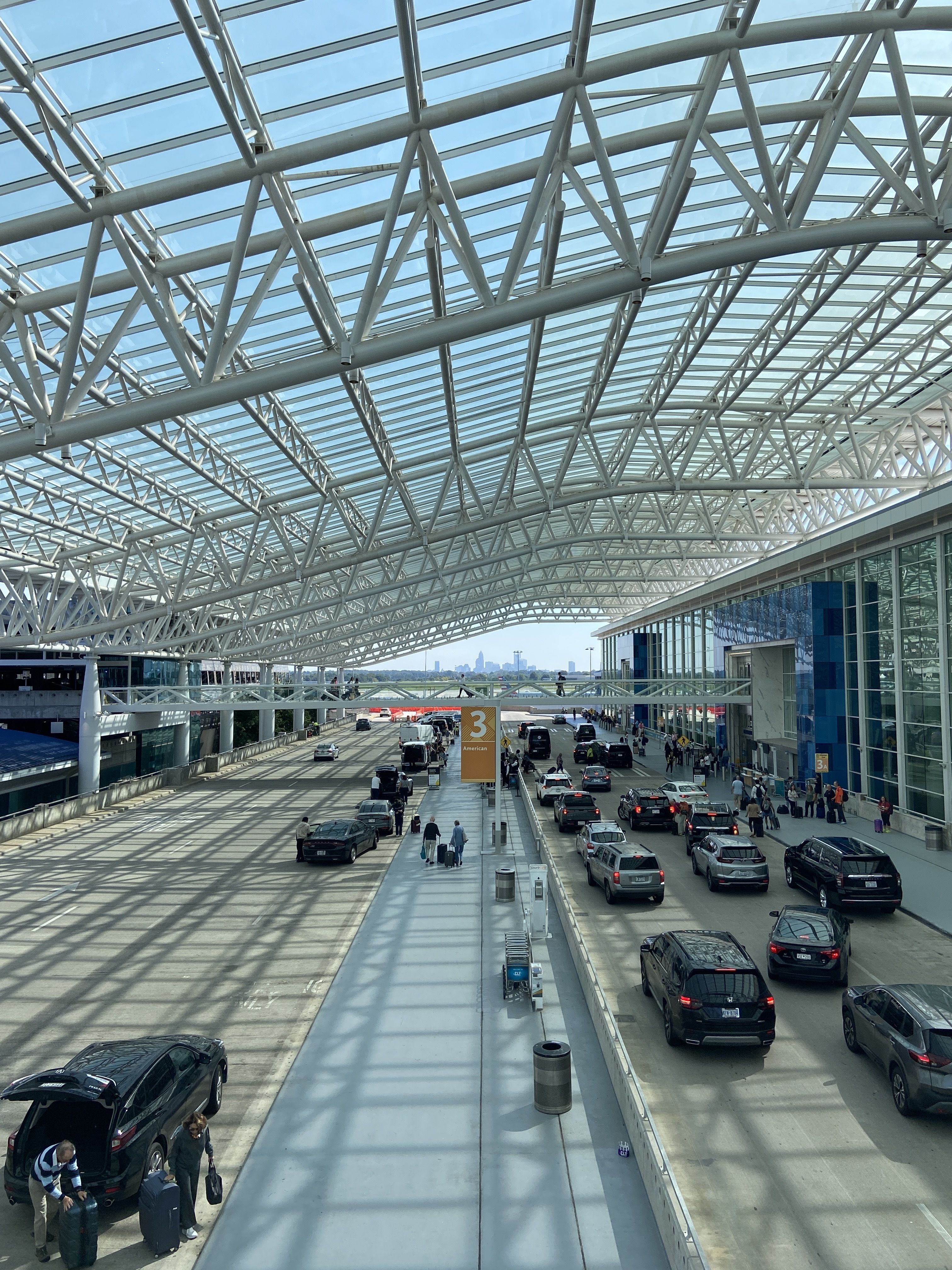The Charlotte skyline can be seen from several parts of the airport, including the skybridges. Cars drive east toward the city under a canopy and skybridges. 