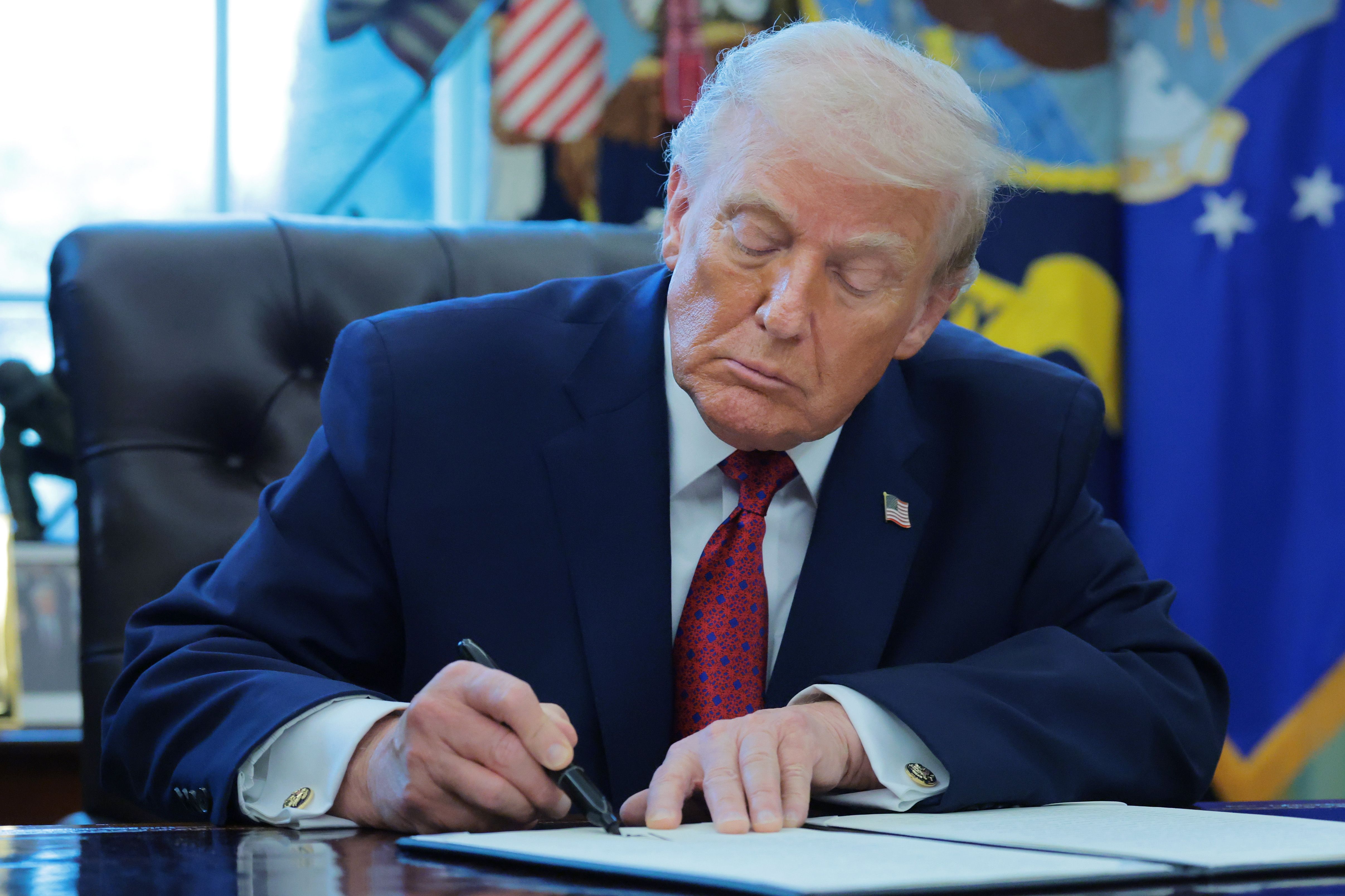 President Donald Trump signs an executive order in the Oval Office as military service members receive the Mexican Border Defense Medal.
