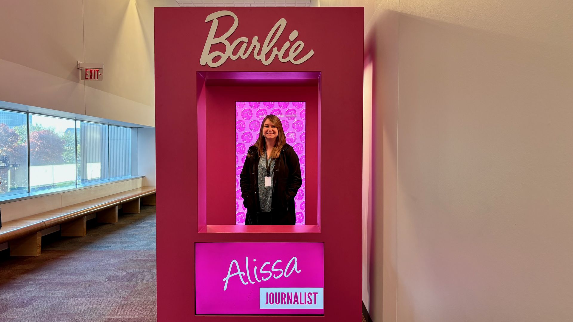Alissa stands in a pink Barbie doll box with a sign on it that says "Alissa - Journalist"