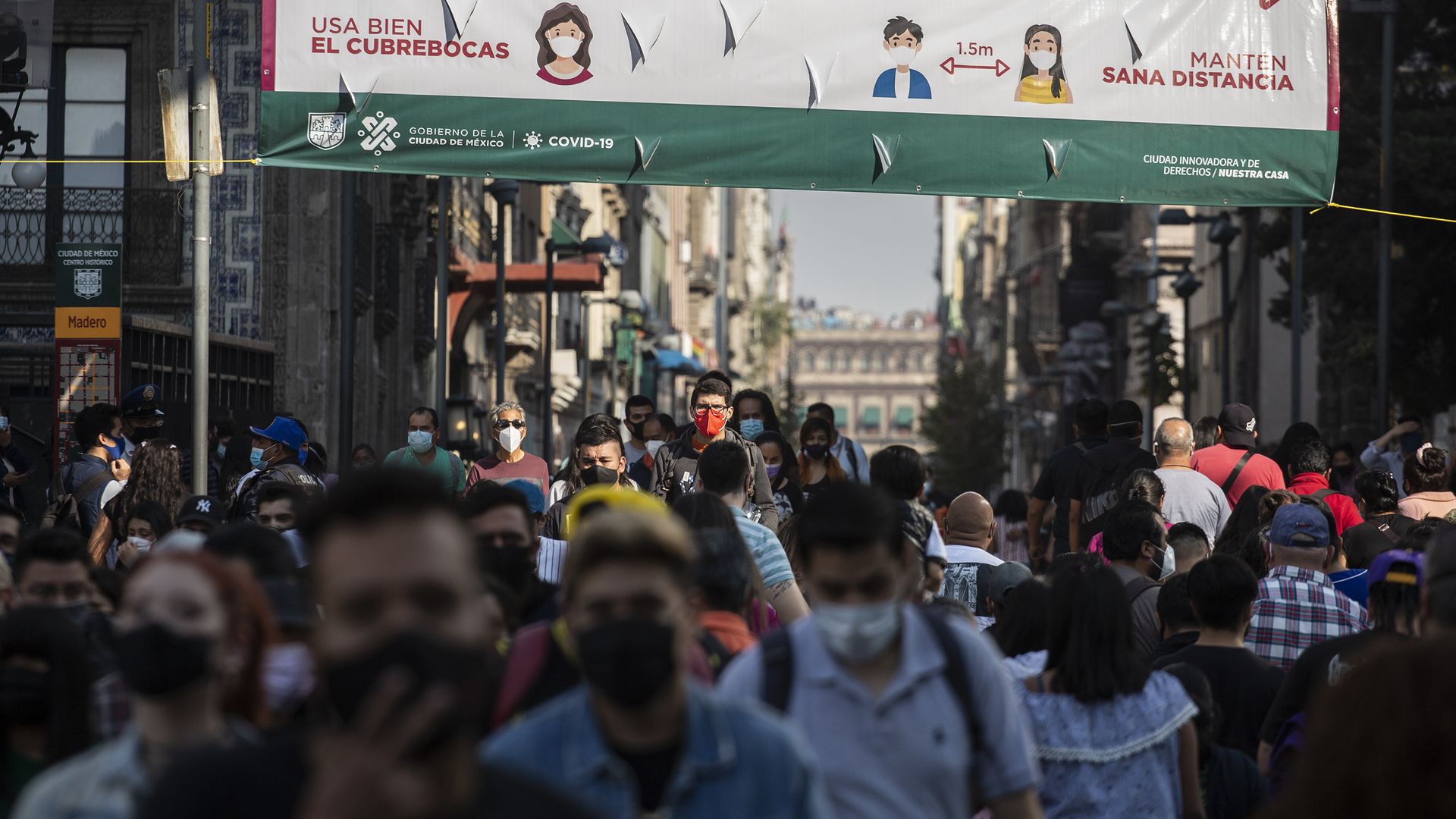 Crowds of people cross an avenue in the historic center as a sign reads 'Avoid masses' on November 14