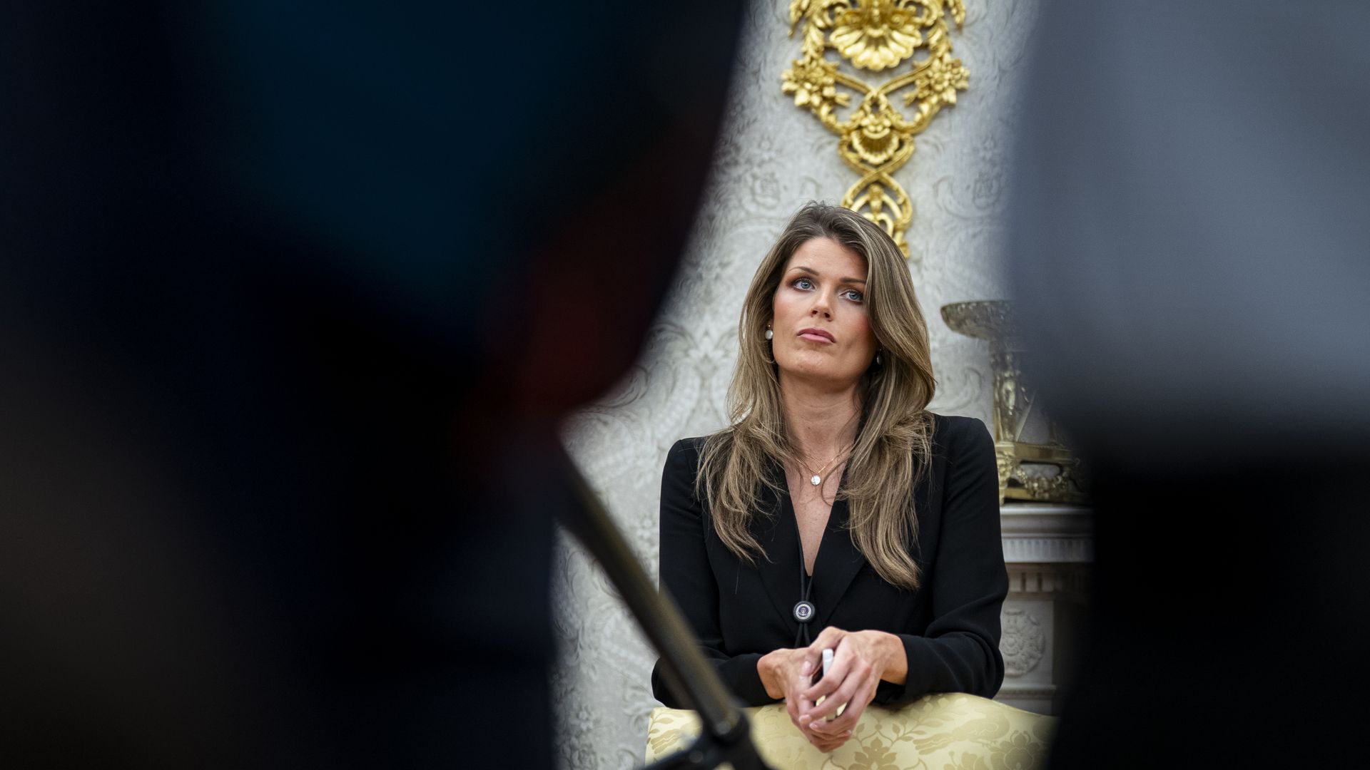 Lindsey Halligan, wearing a black top, holds her hands together and looks on while in the Oval Office.