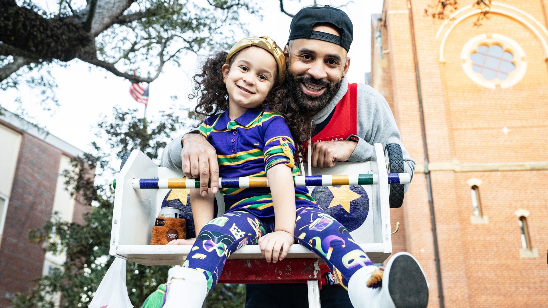 A man and a girl smile at the top of Mardi Gras ladder