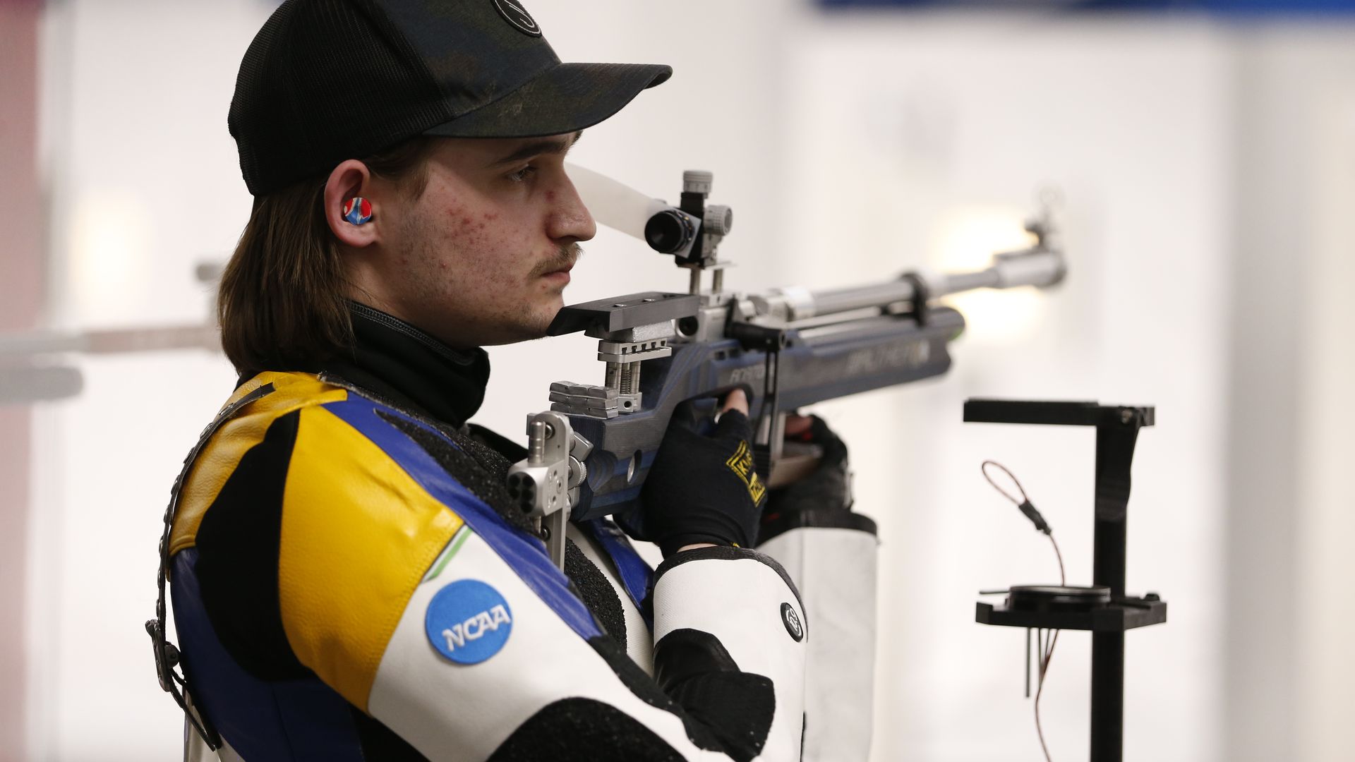 A man in a baseball cap holds a rifle. 