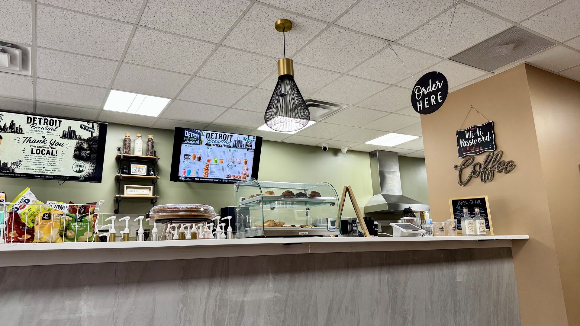 A coffee counter with syrups and baked goods and a menu in the background