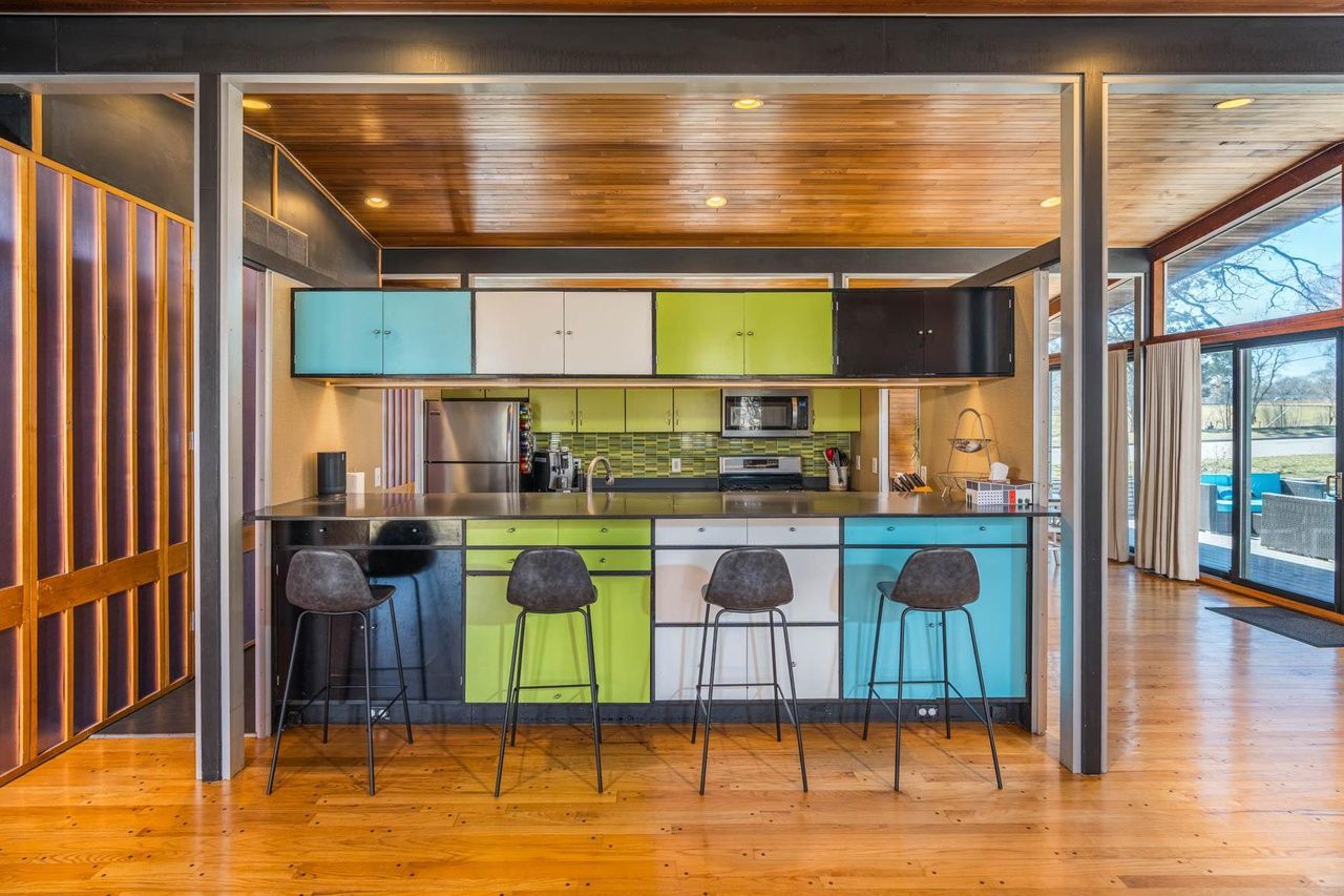 A mid-century modern style home with wooden ceilings and green, white anmd blue cabinets in the kitchen.