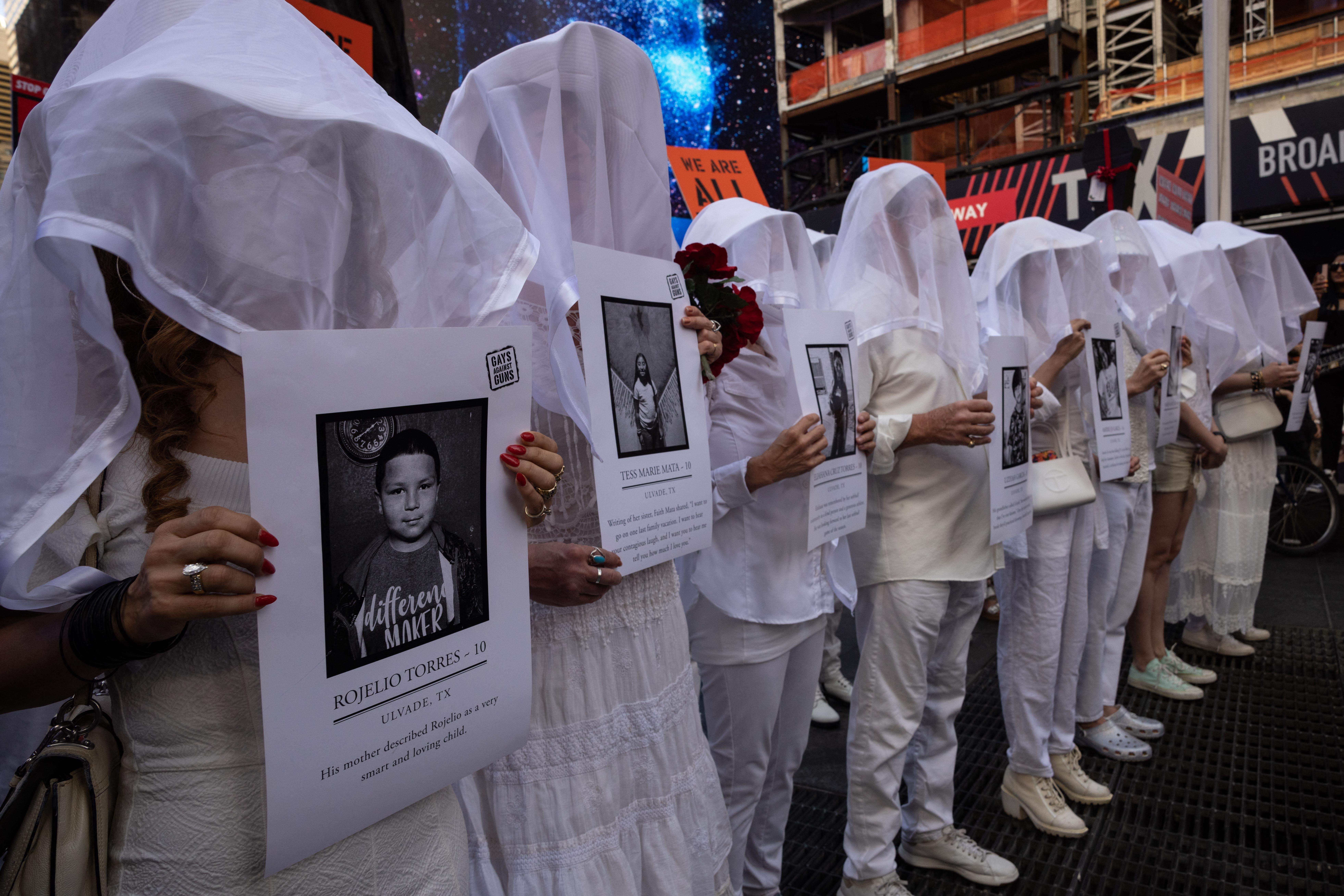 Photo of people dress in white and wearing veils as they hold pictures of victims of the Uvalde shooting