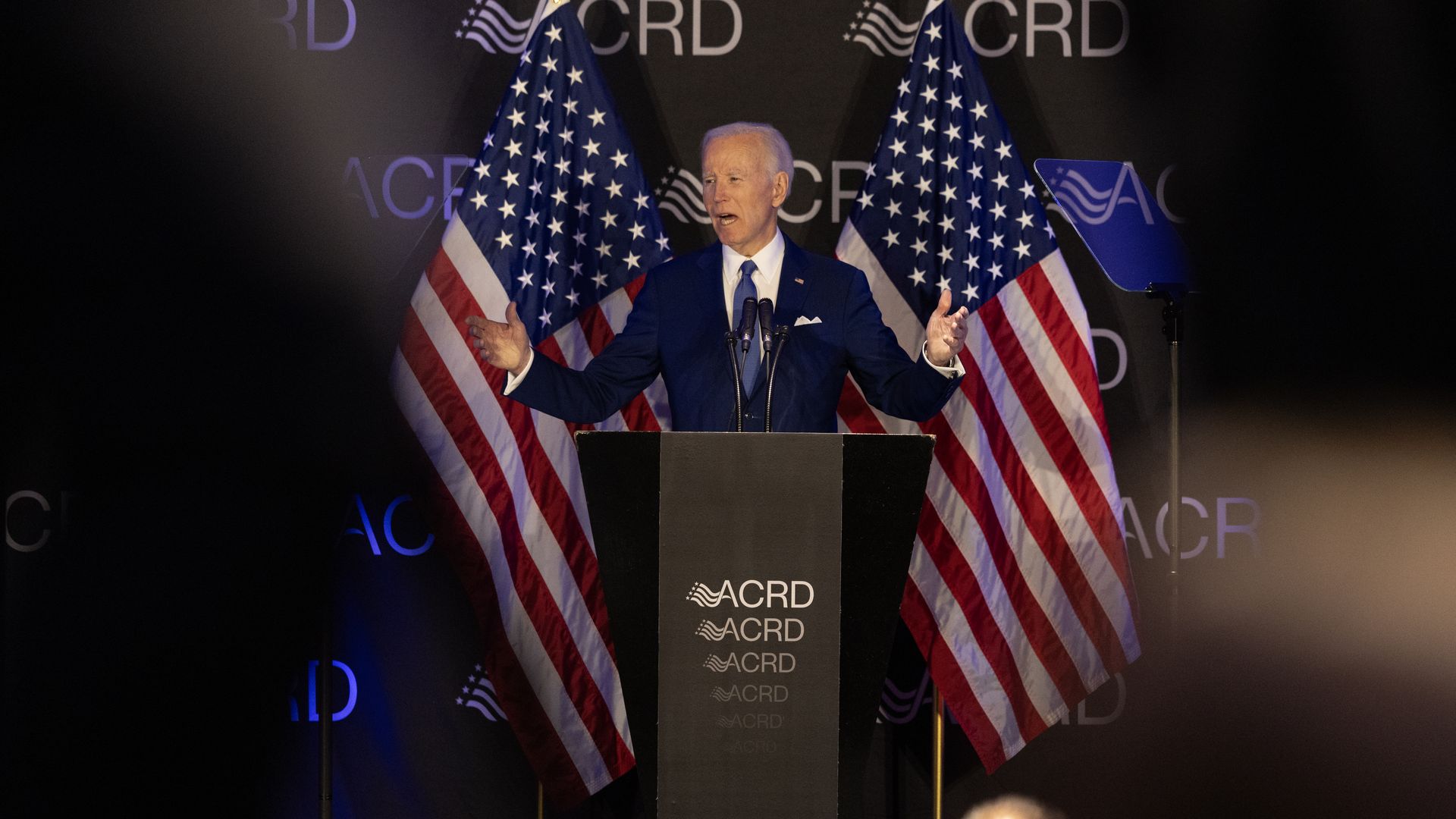 Joe Biden gestures as he speaks at an event in front of two American flags.