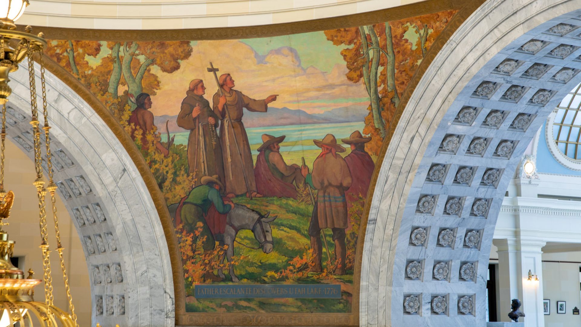 Curved-wall interior mural of explorers and Native Americans by a lakeside, with a priest pointing, one holding a cross; reads "Father Escalante Discovers Utah Lake 1776".