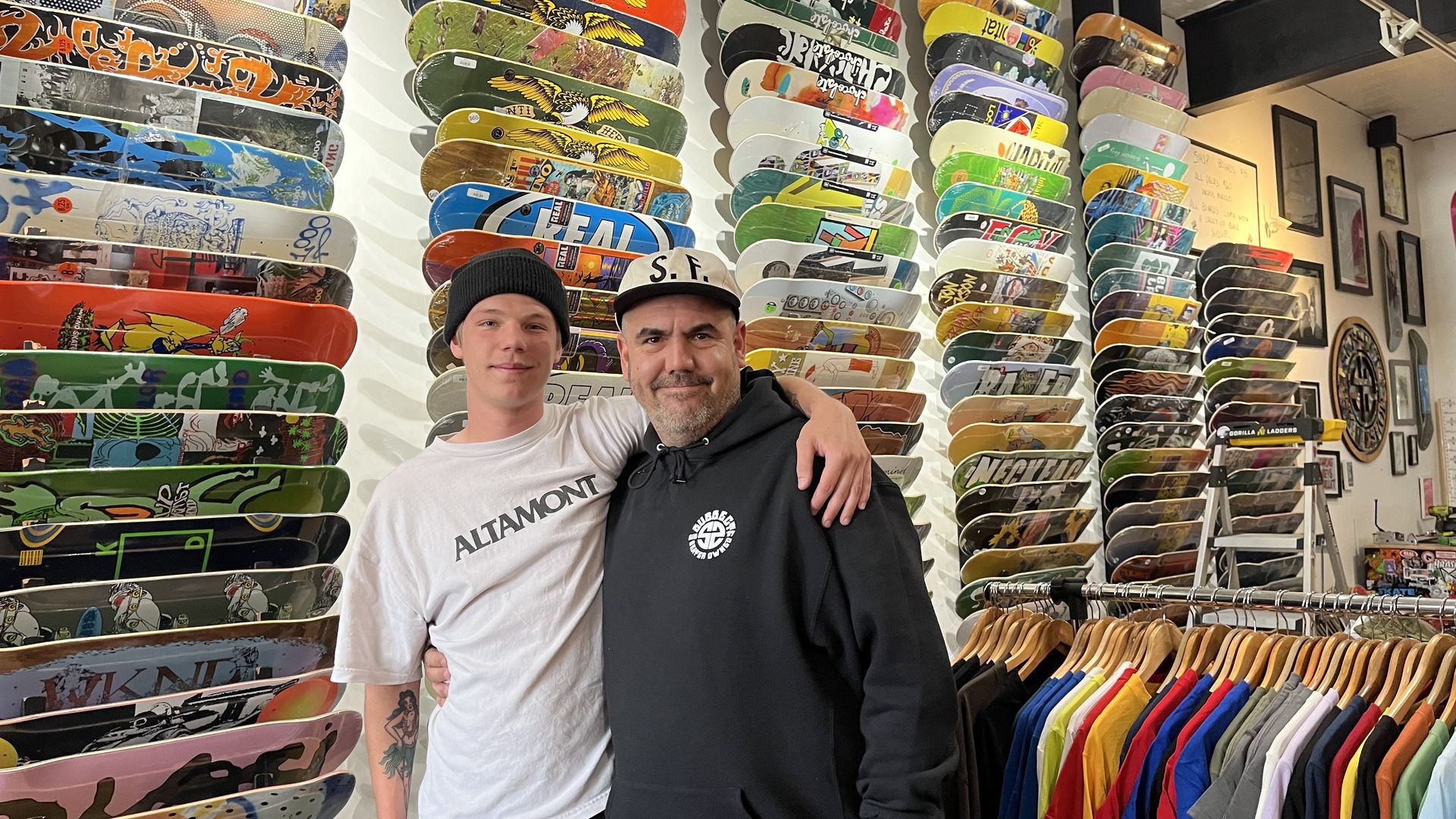 The owner of the skate shop Kevin jones and one of his employees in front of a wall of skateboard in the shop
