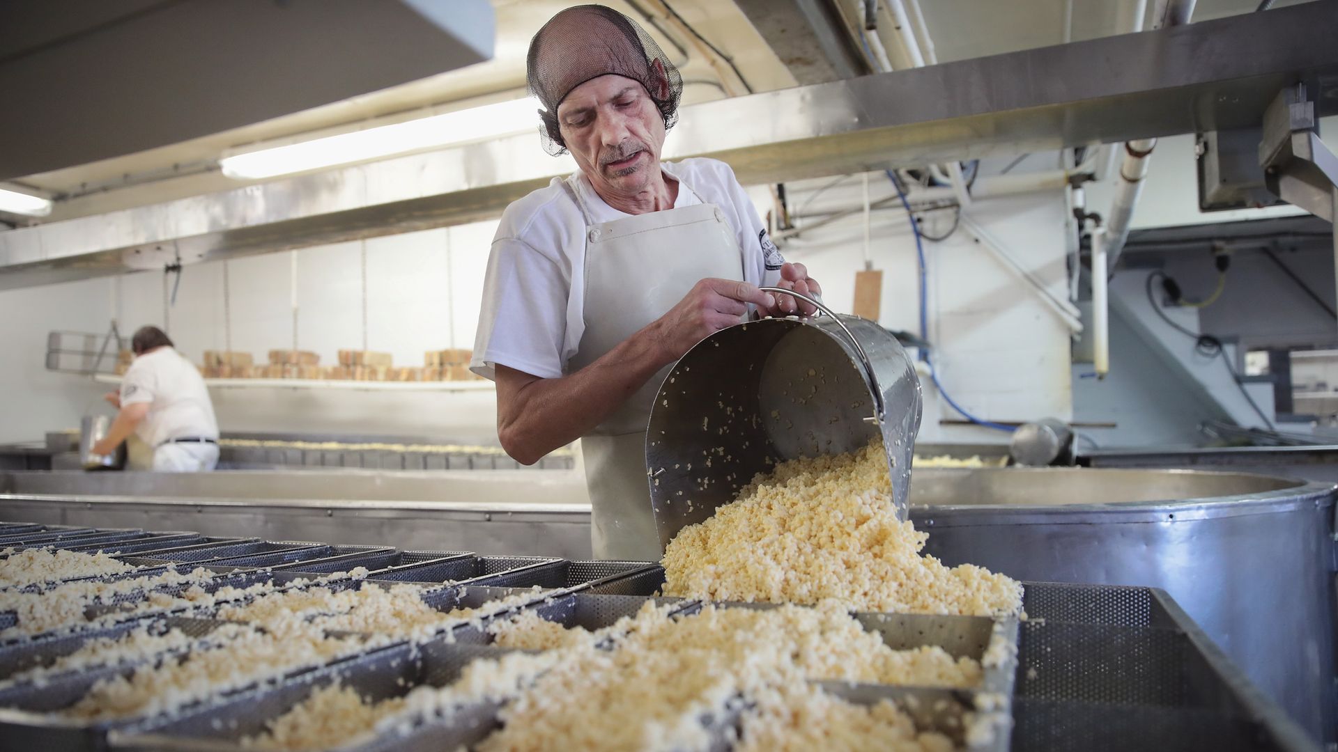 A man pours shredded cheese from a massive pot 