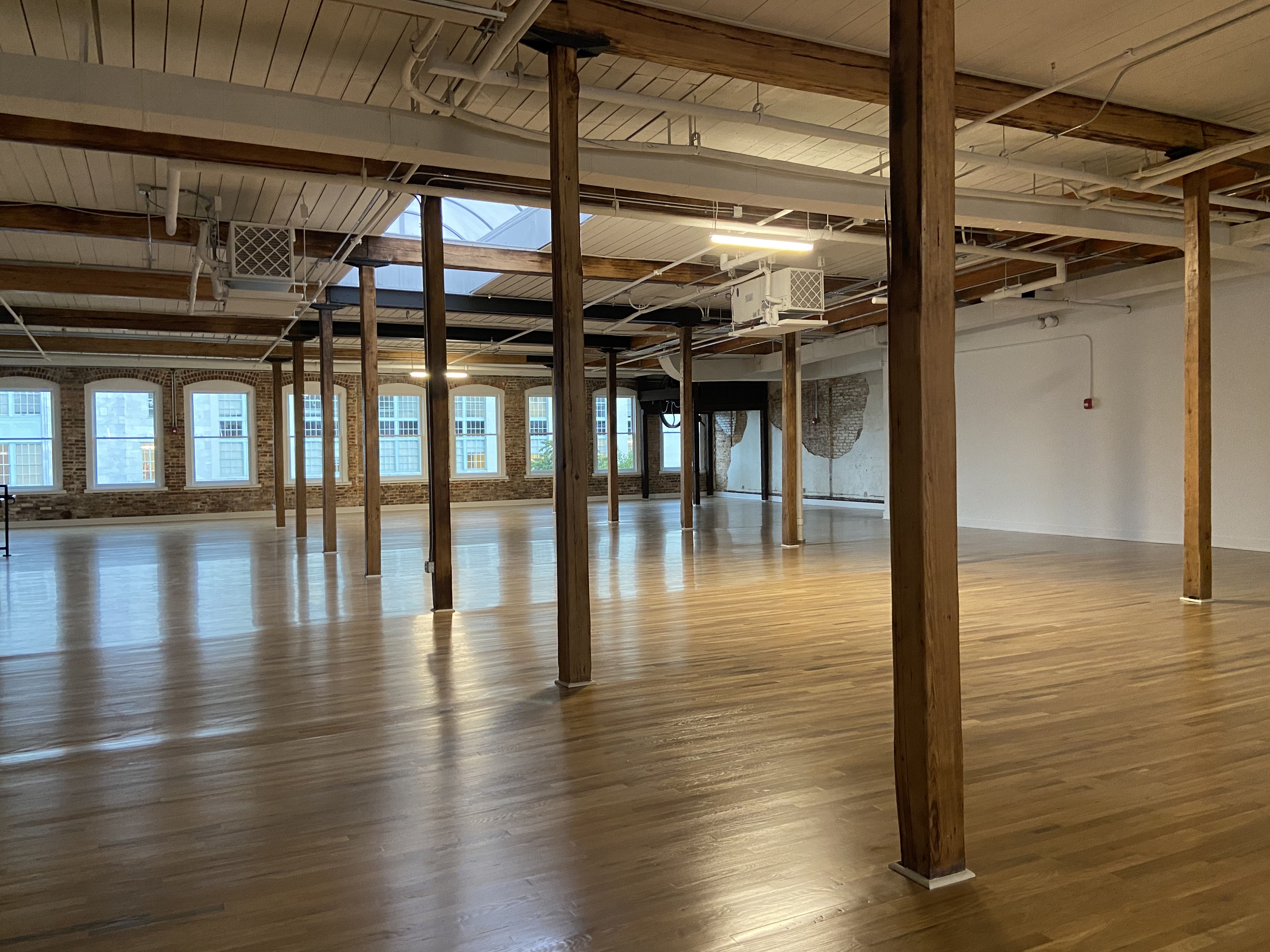The interior of a extra-large open-floor office space with hardwood floors, illuminated by a skylight 