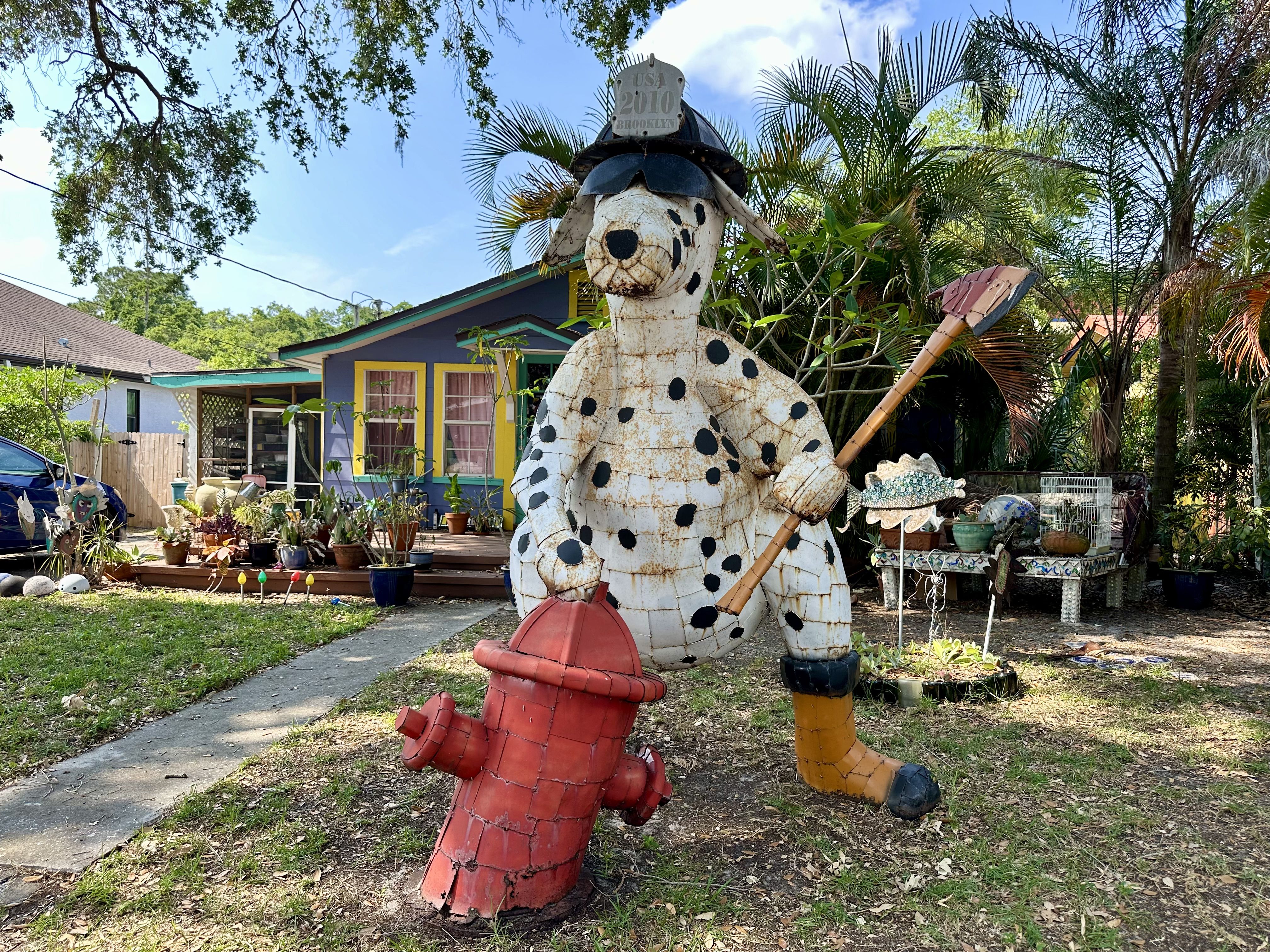 a metal statue of a dalmatian wearing a firefighter's helmet and sunglasses, holding an axe in front of a fire hydrant