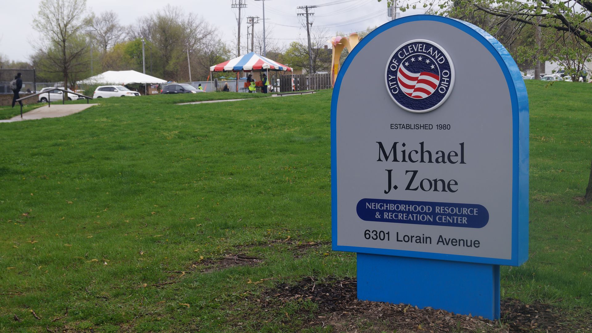 A sign for Michael J. Zone Recreation Center with a line of cars in the background